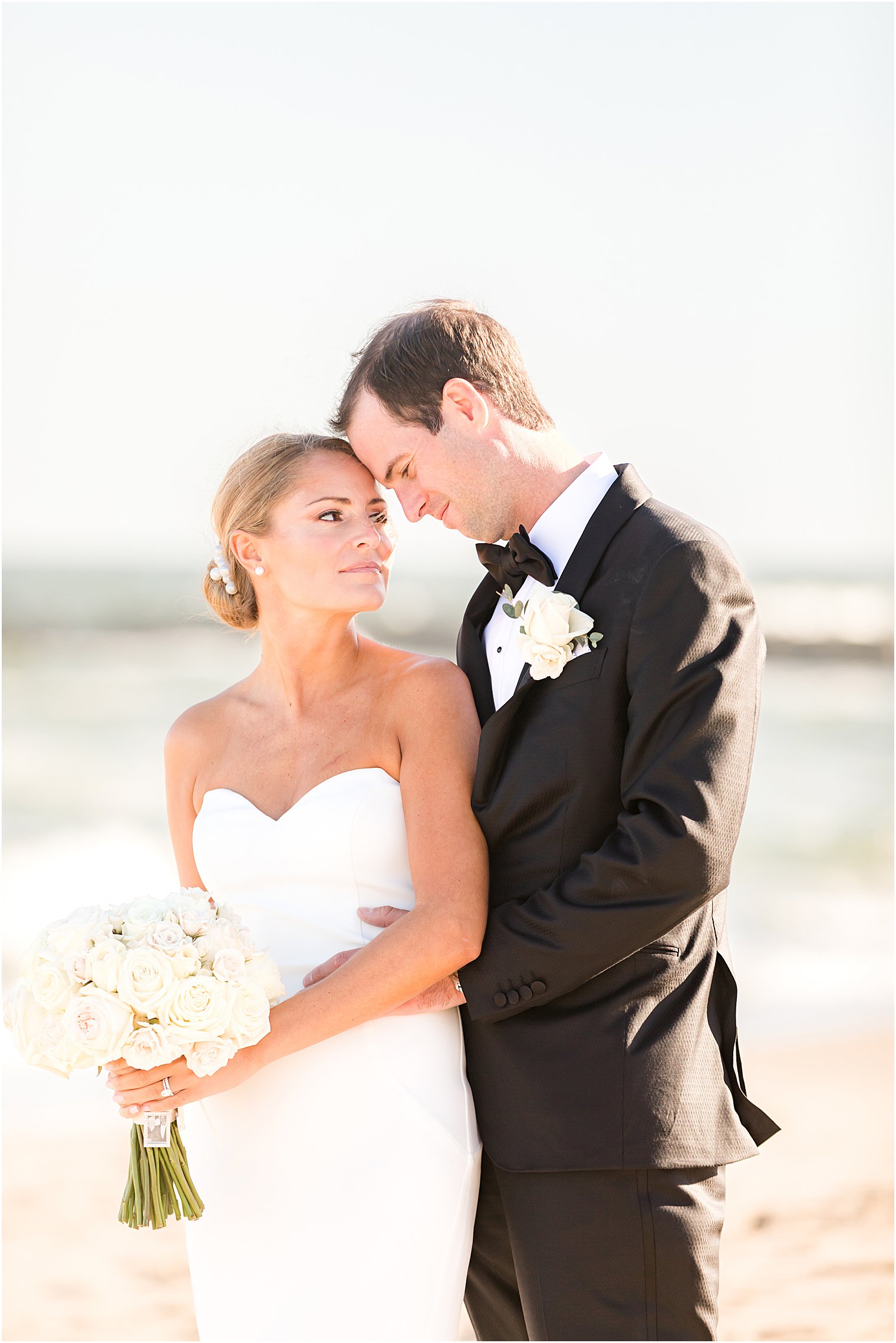 bride and groom lean together on sand in Asbury Park