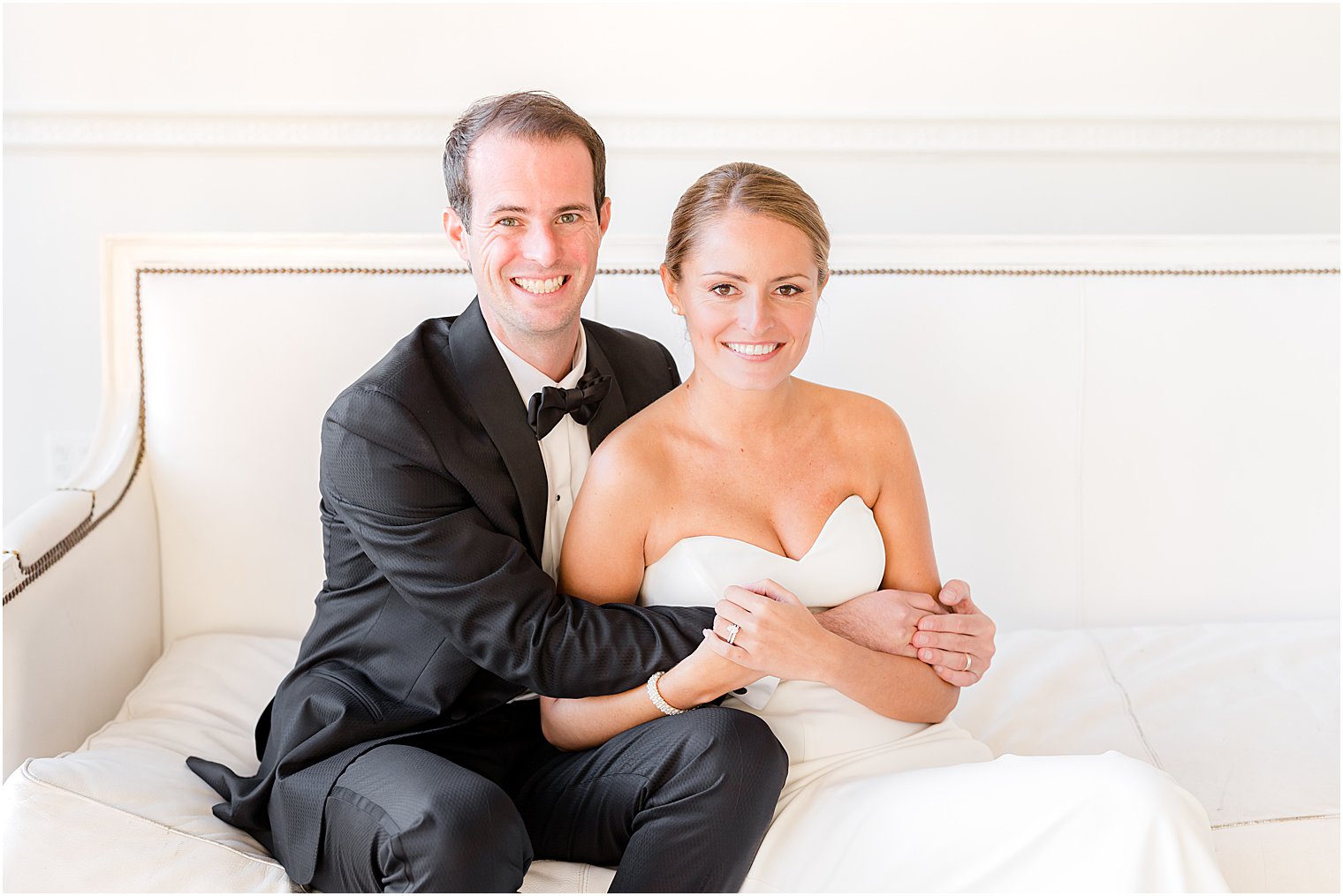 groom hugs bride to him on white bench inside the Berkeley Oceanfront Hotel