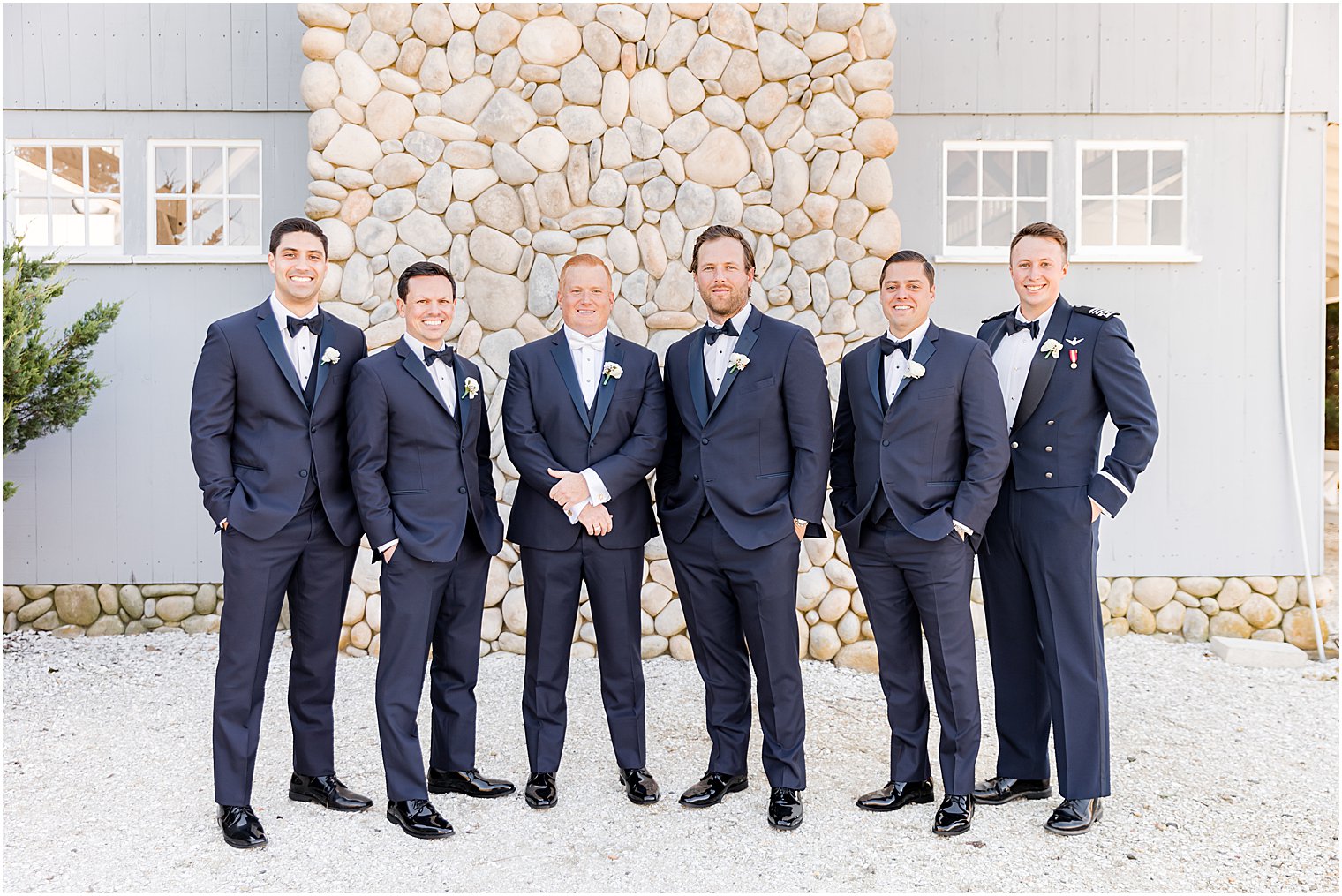 groom poses with groomsmen in navy suits outside stone fireplace at Bonnet Island Estate 
