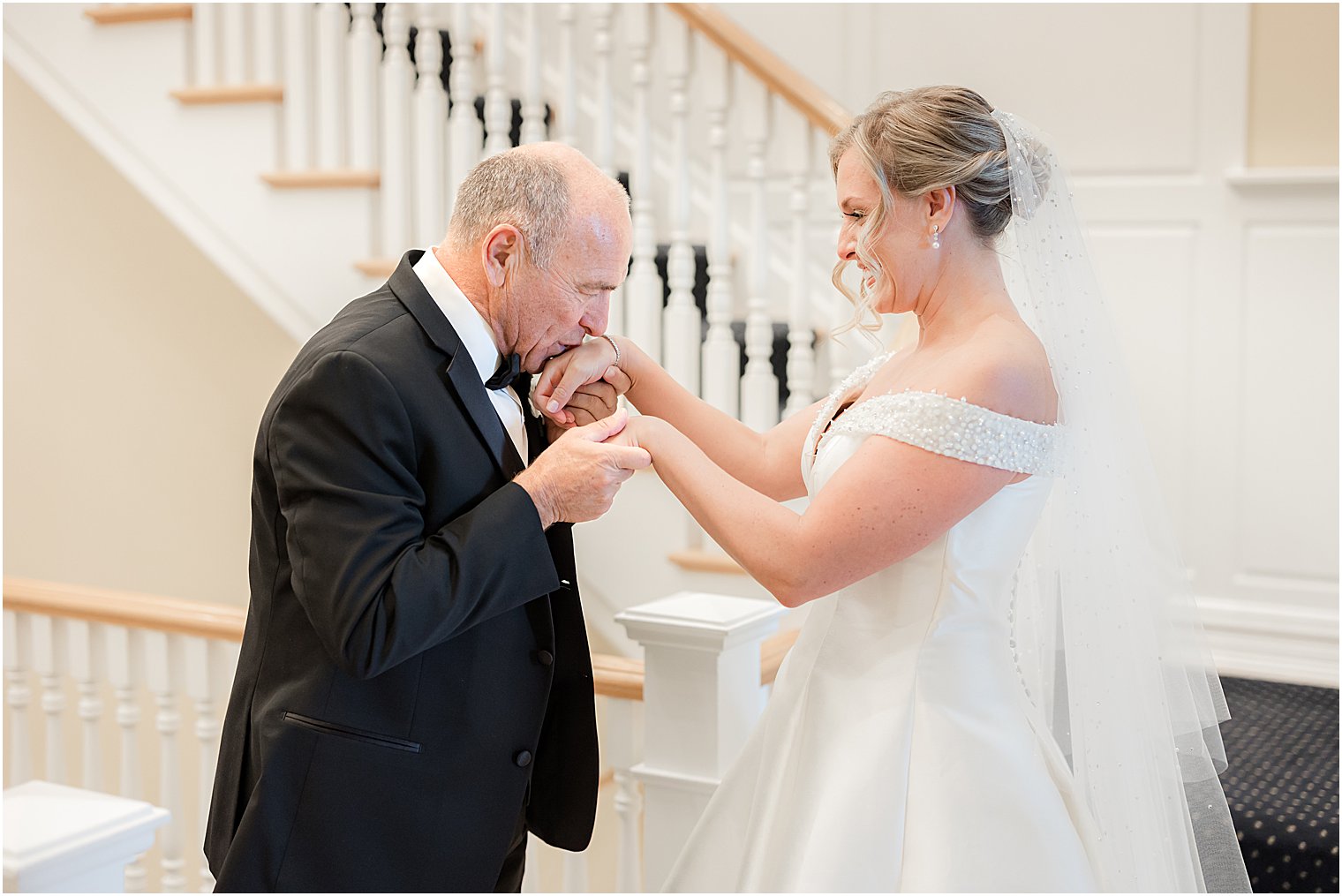 dad in tux kisses bride's hand during first look on staircase 