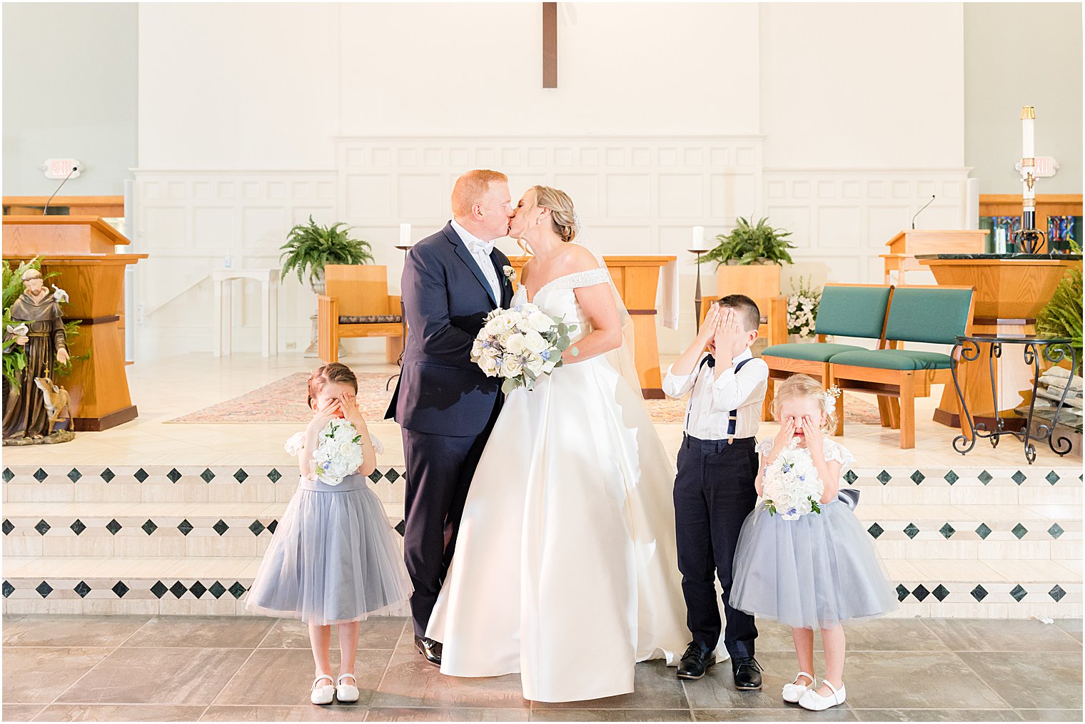 bride and groom kiss while ring bearer and flower girls cover eyes 