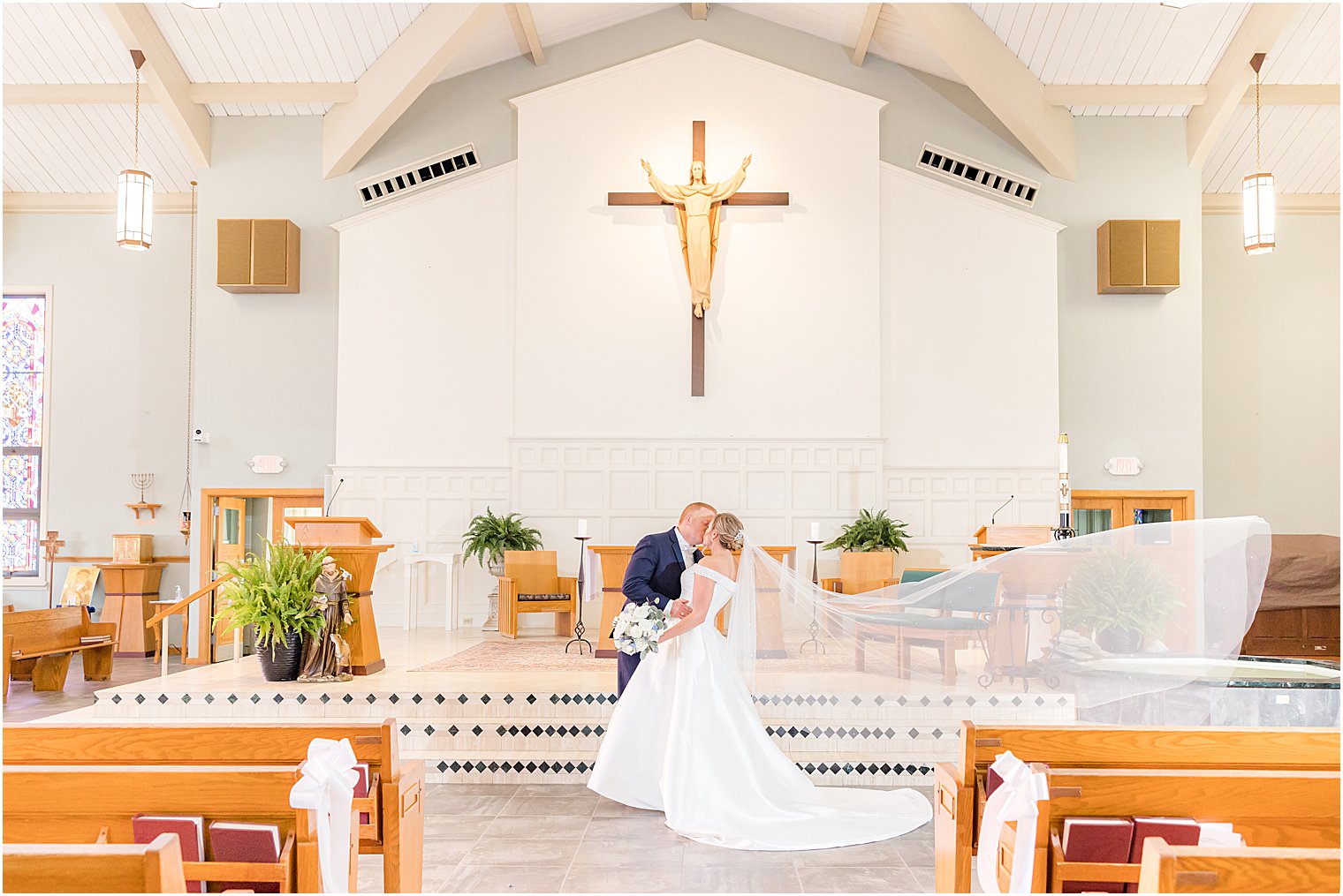 bride and groom kiss at alter with veil floating in church 