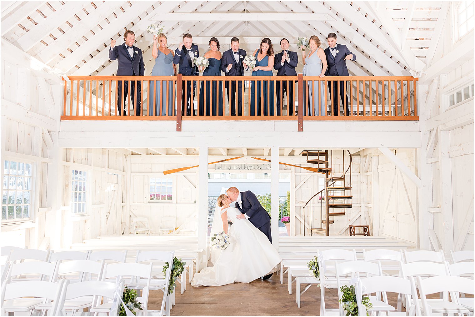 wedding party cheers from balcony as bride and groom kiss in chapel