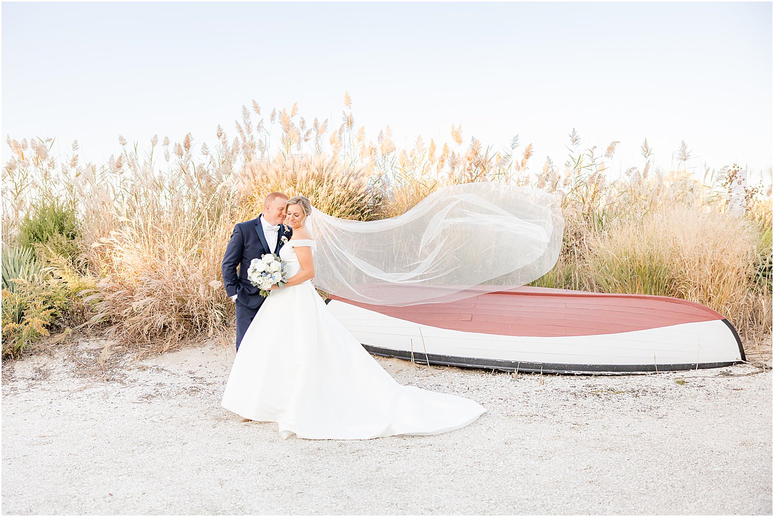 groom nuzzles bride's cheek as veil floats standing by canoe 
