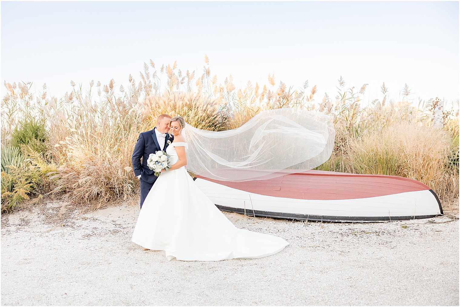 groom nuzzles bride's cheek as veil floats standing by canoe