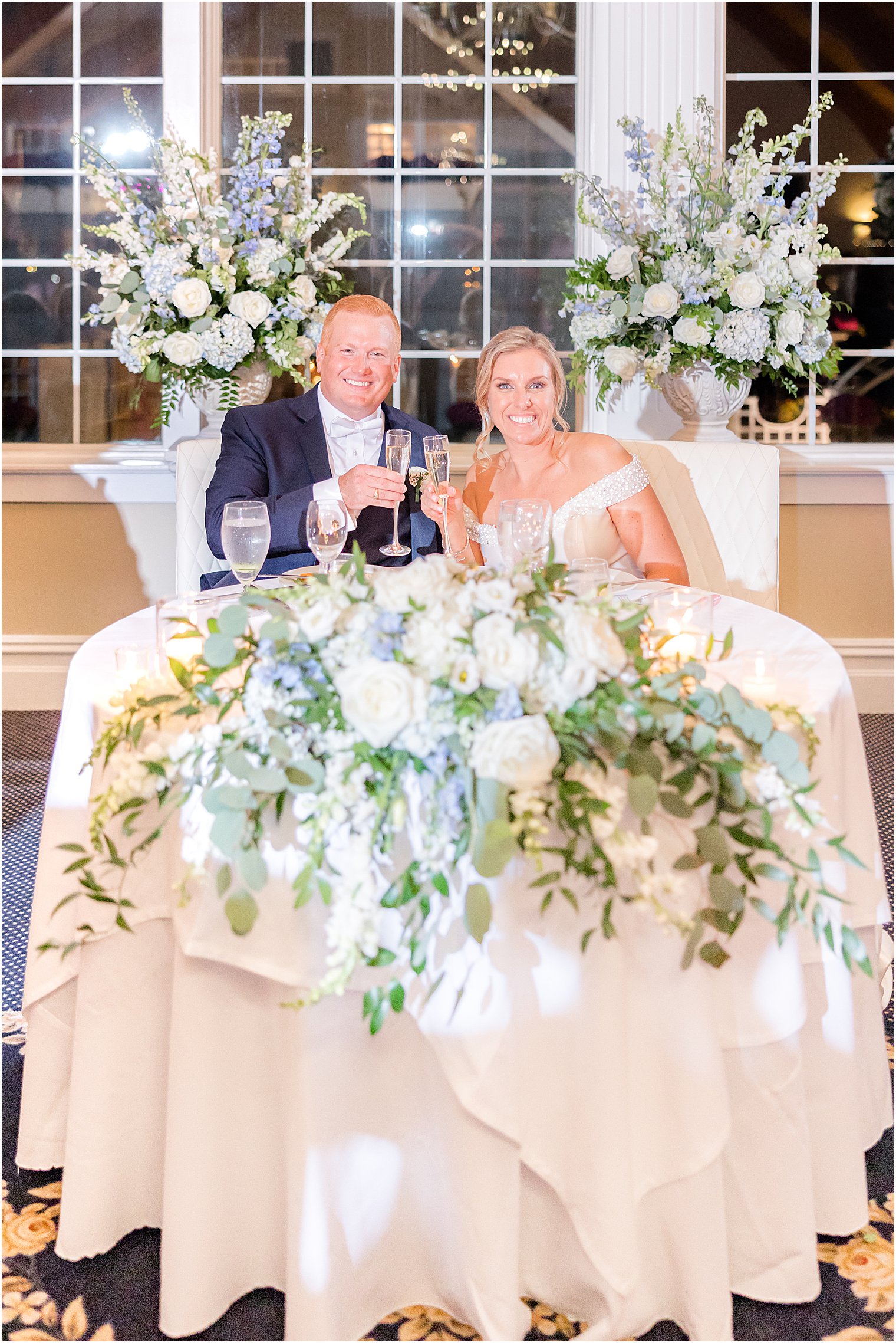 bride and groom sit at sweetheart table with white and blue floral details 