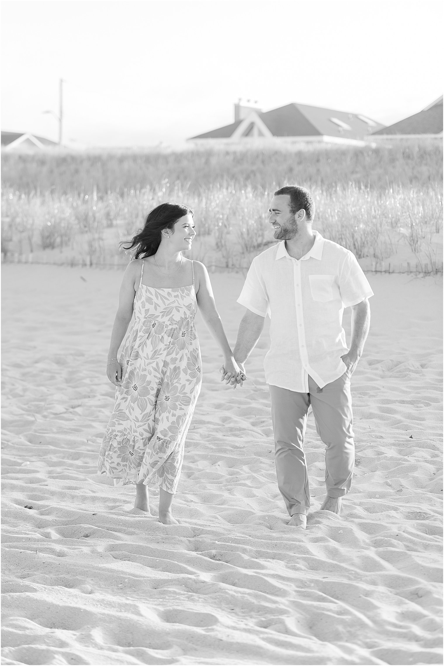 couple holds hands walking on sand at Lavallette Beach