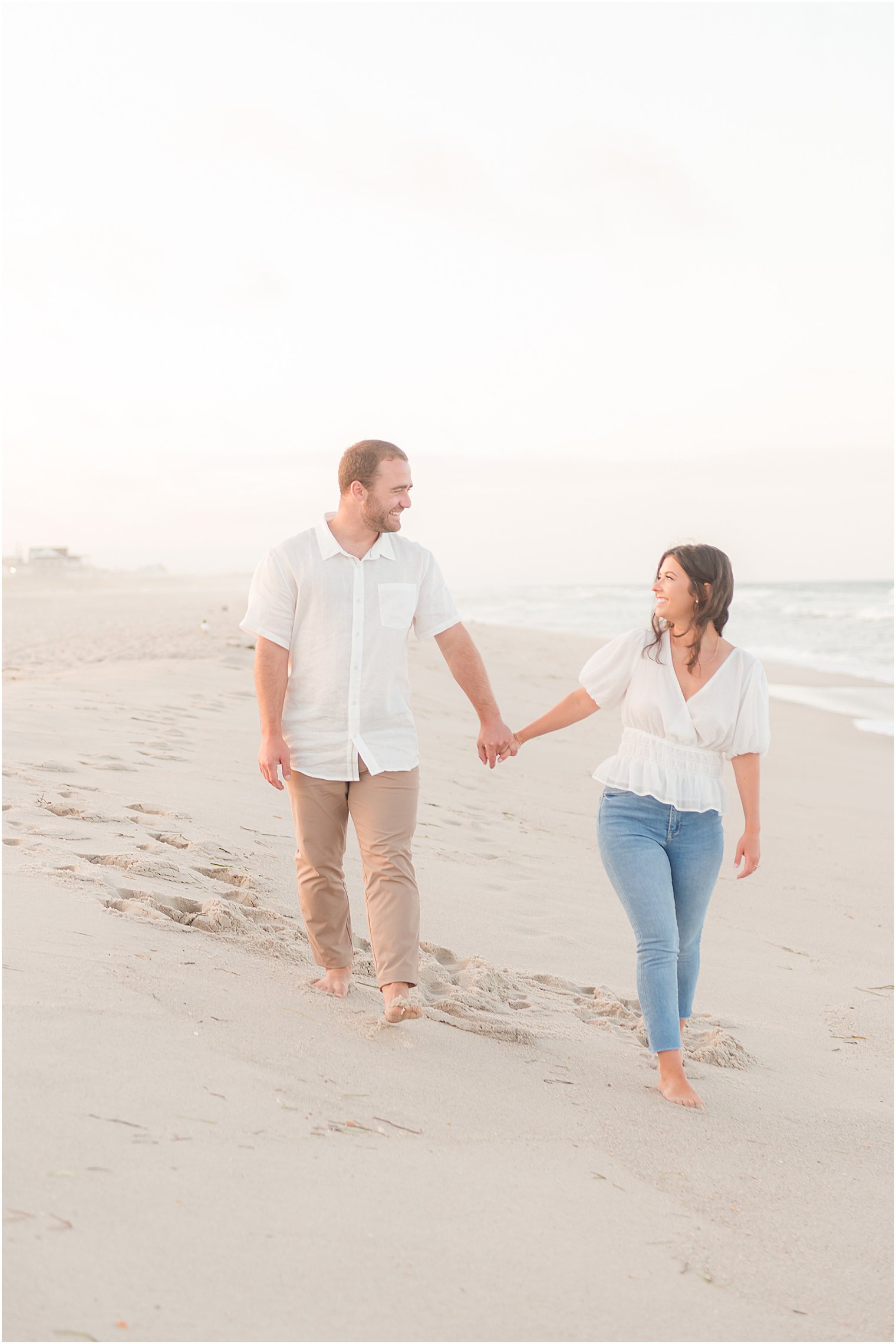 couple holds hands walking on Jersey beach