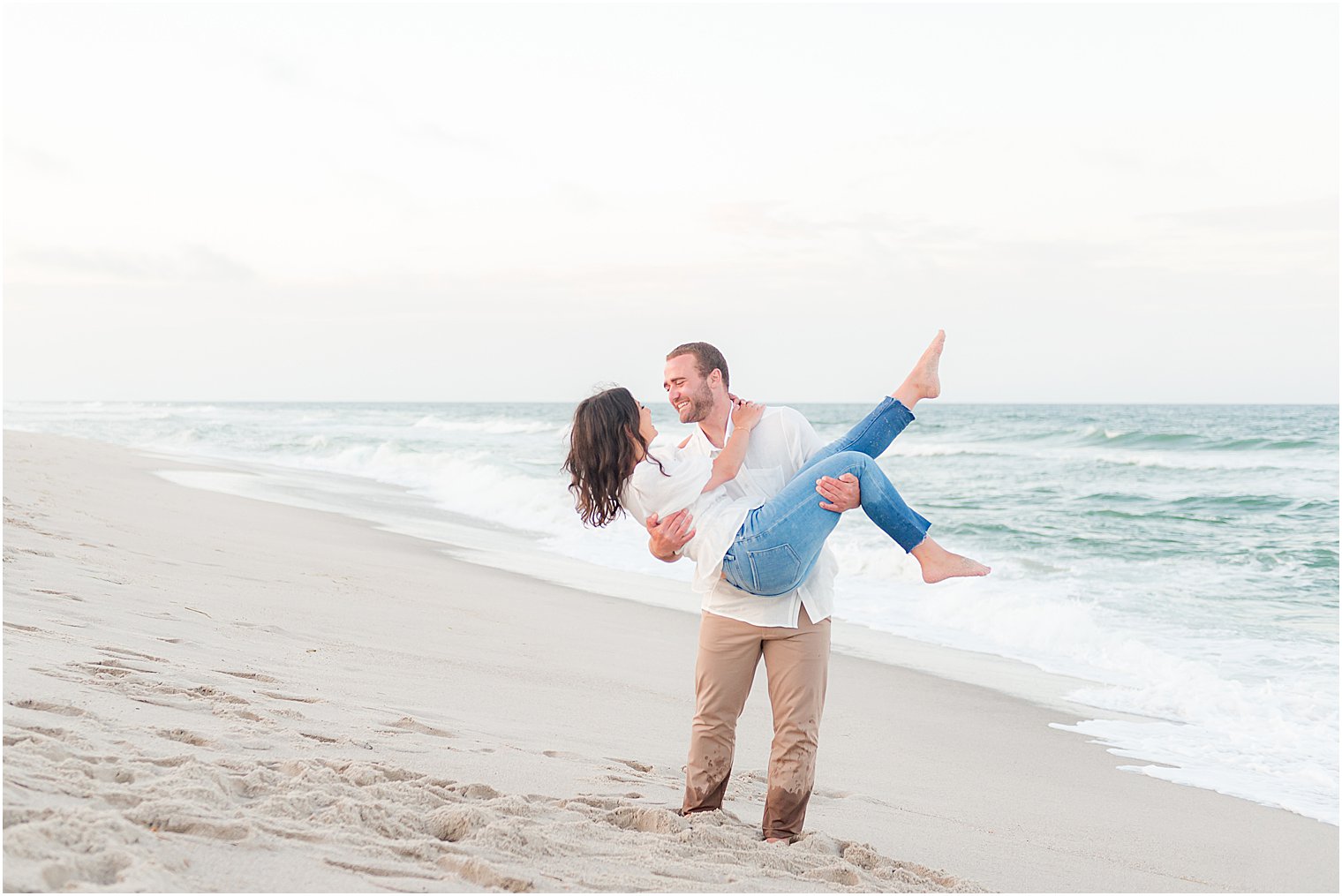 groom lifts bride on beach smiling at her