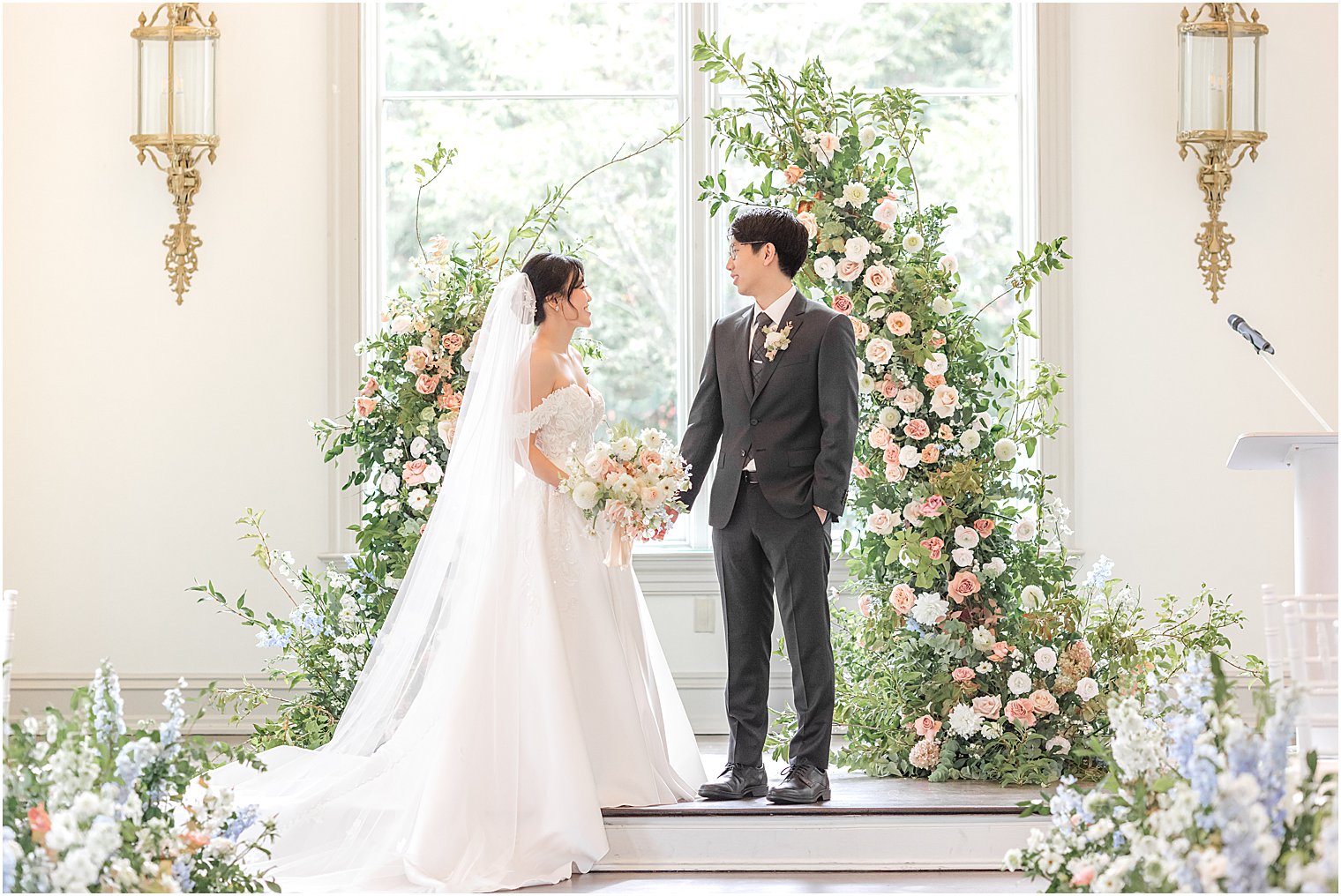 bride and groom pose by floral display in chapel at Park Chateau Estate