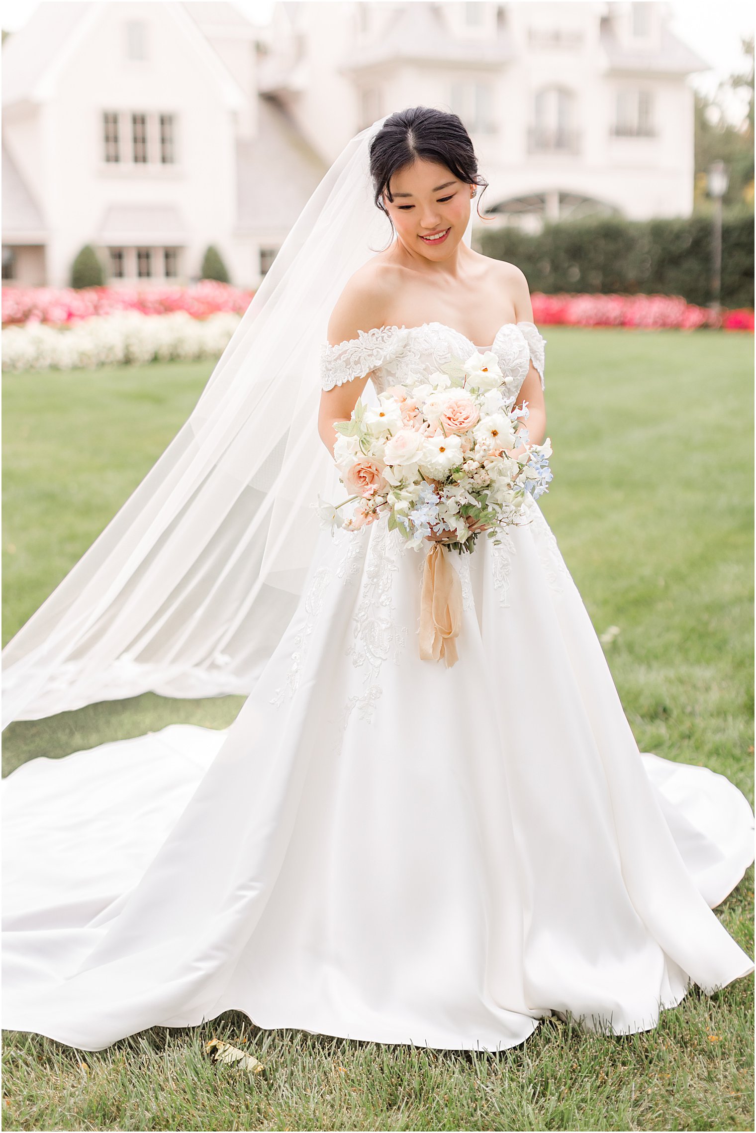 bride stands on lawn at Park Chateau Estate with bouquet of pink and white flowers 
