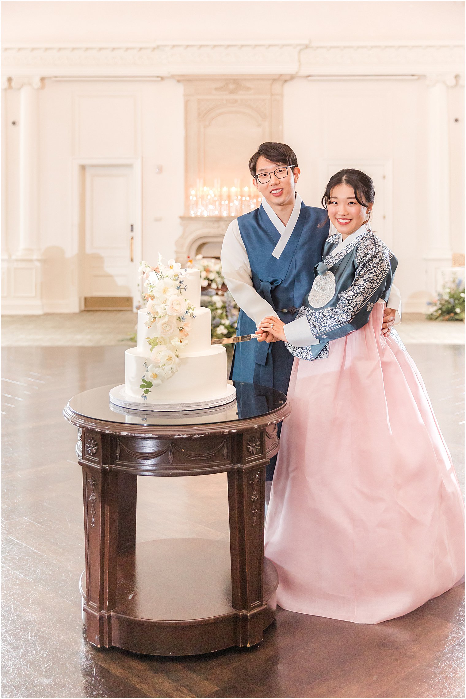 bride and groom pose with wedding cake in traditional Korean outfits