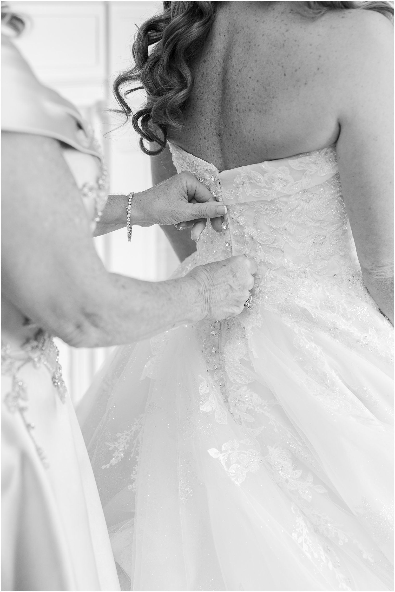 black and white photo of mother buttoning up bride's gown