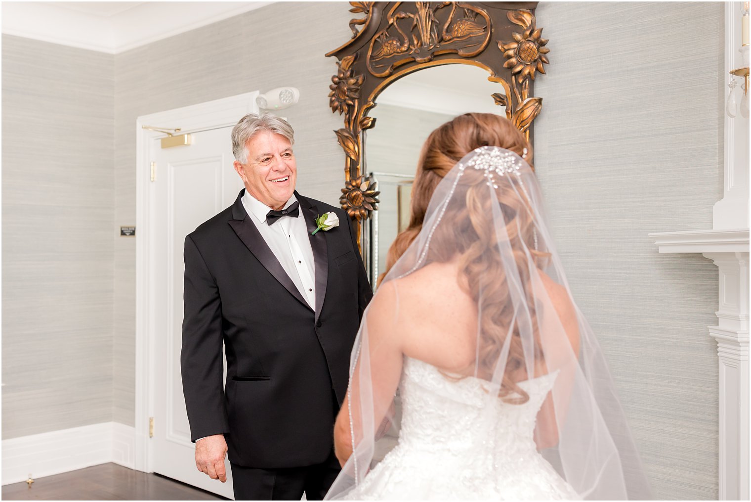 dad in tux smiles at bride during first look in bridal suite 