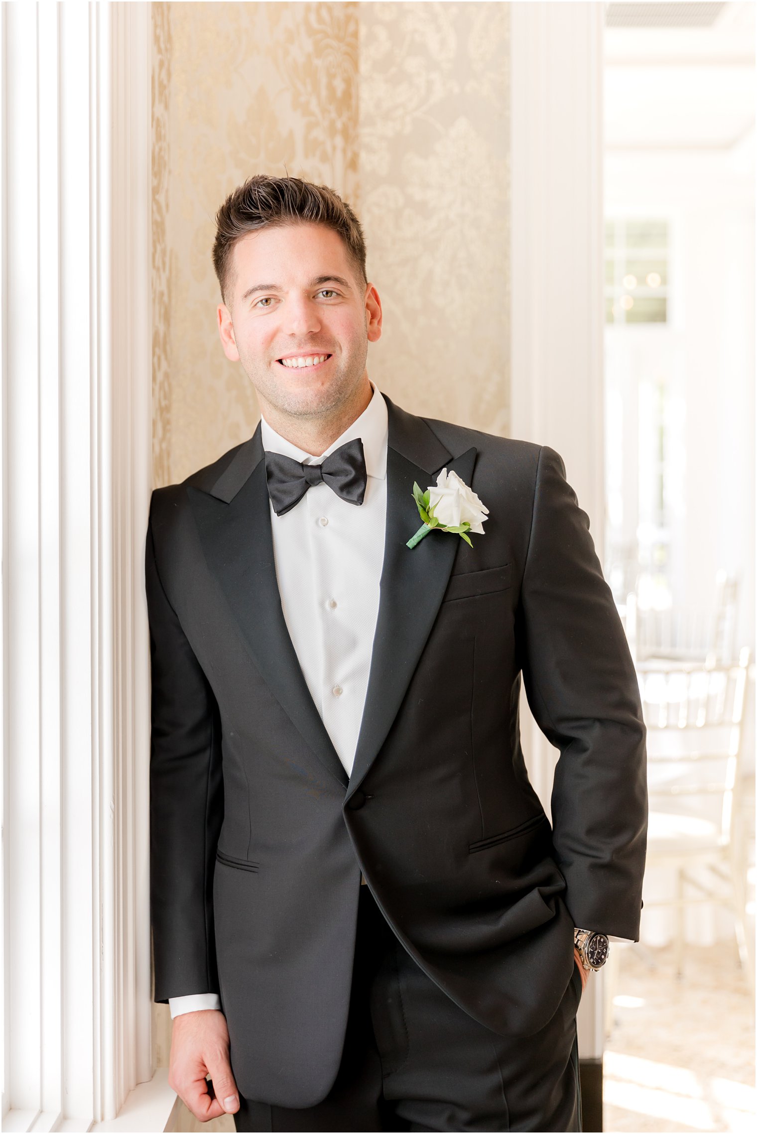 groom leans against wall in Shadowbrook at Shrewsbury in classic black tux