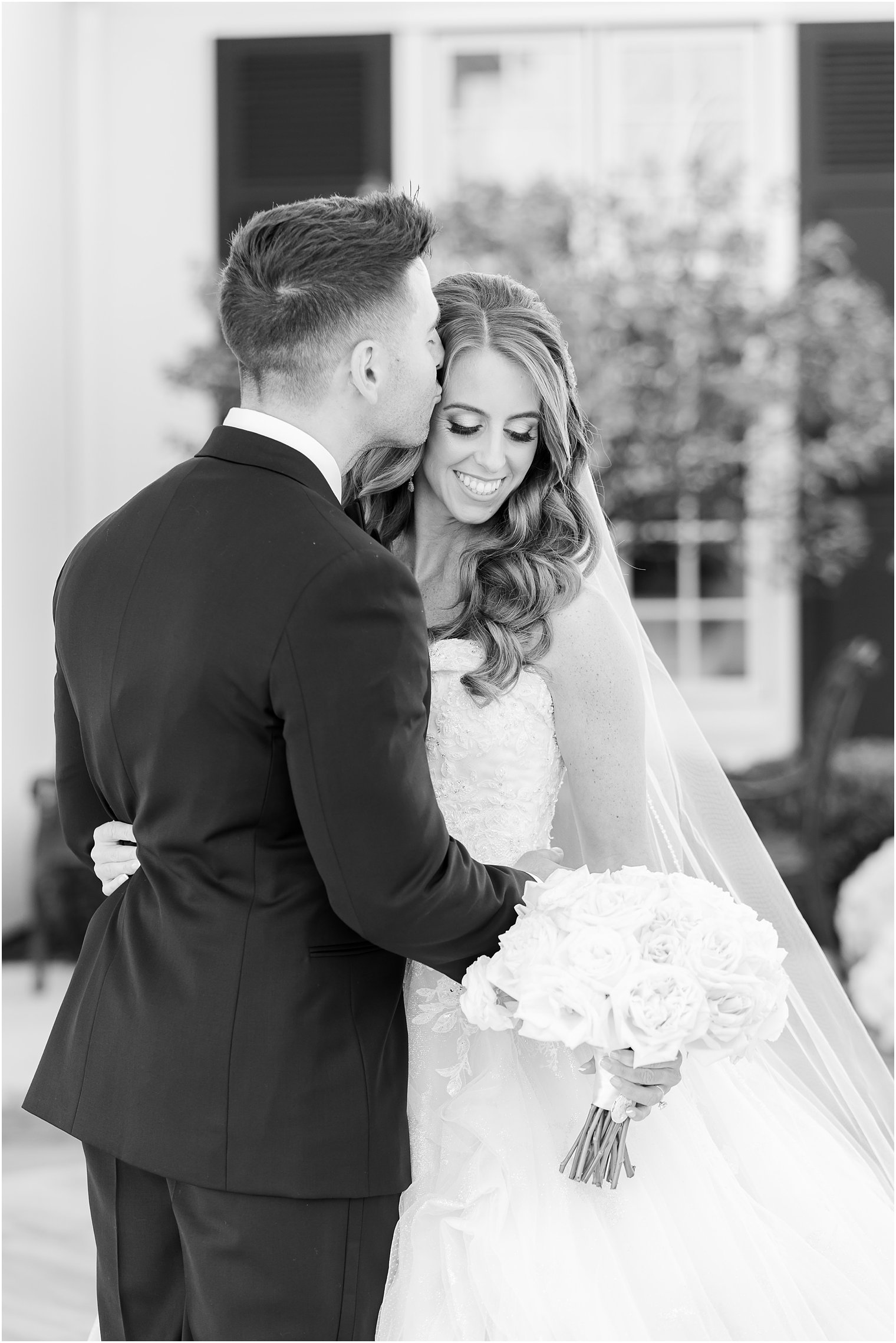 groom kisses bride's forehead during portraits in front of Shadowbrook at Shrewsbury