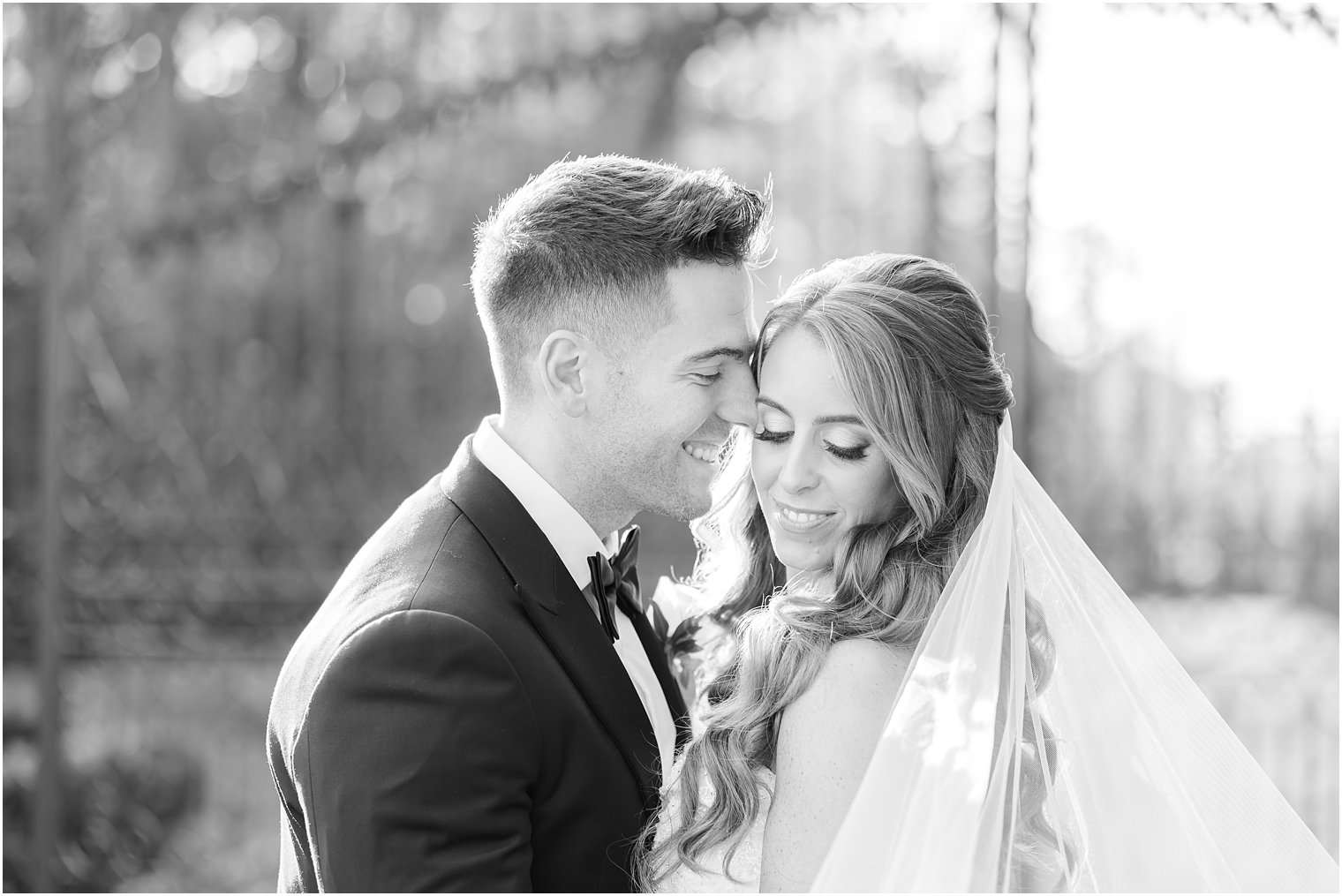 groom leans to nuzzle bride's cheek by gates at Shadowbrook at Shrewsbury