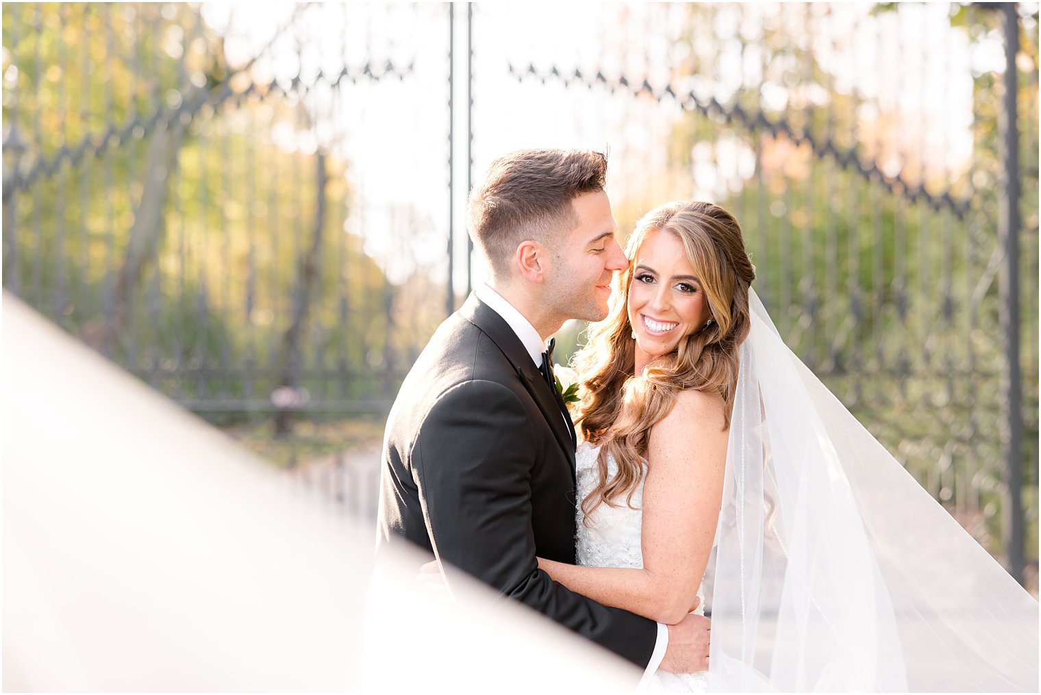 groom leans to kiss bride's cheek while veil drapes in front of them at Shadowbrook at Shrewsbury