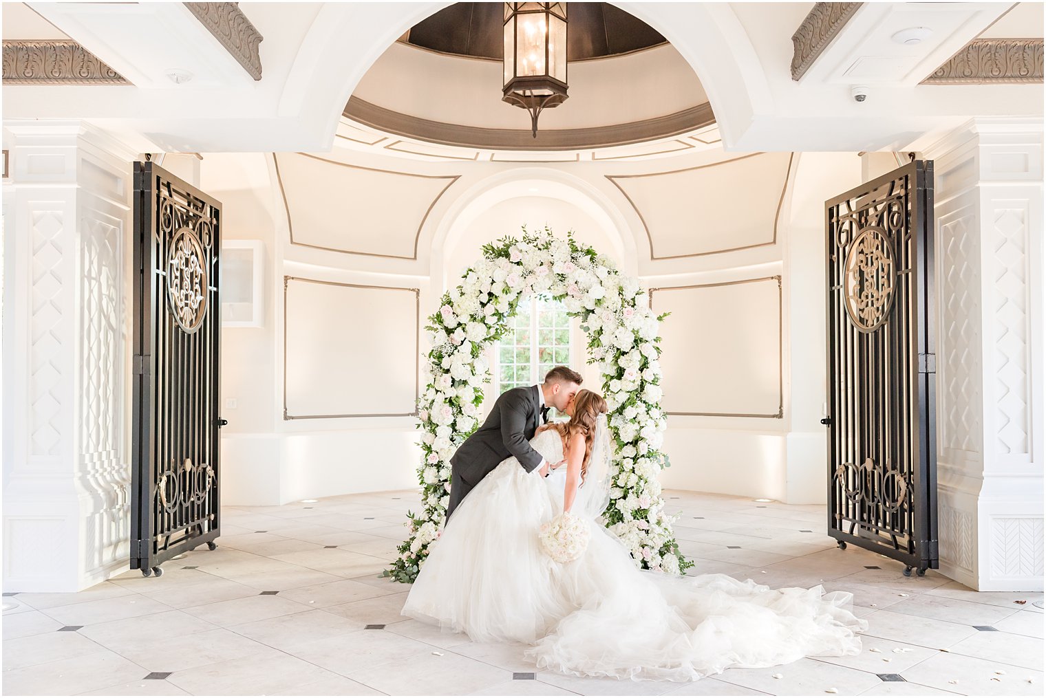 groom kisses bride by trellis of white roses at Shadowbrook at Sherwsbury