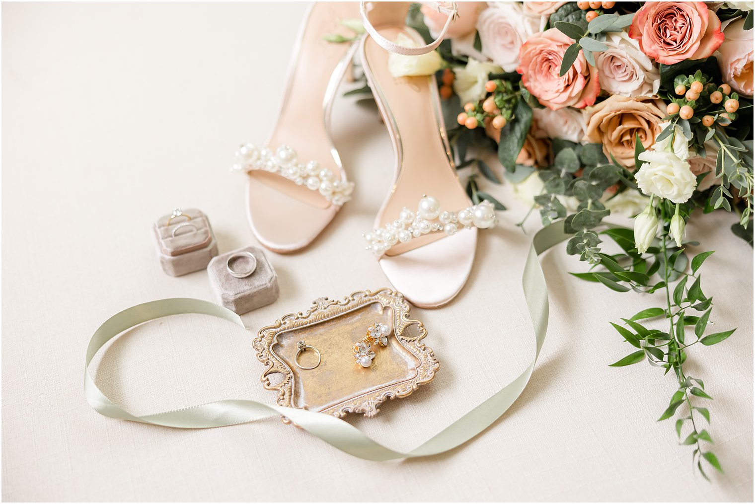 bride's shoes rest by gold jewelry tray and pearl earrings 