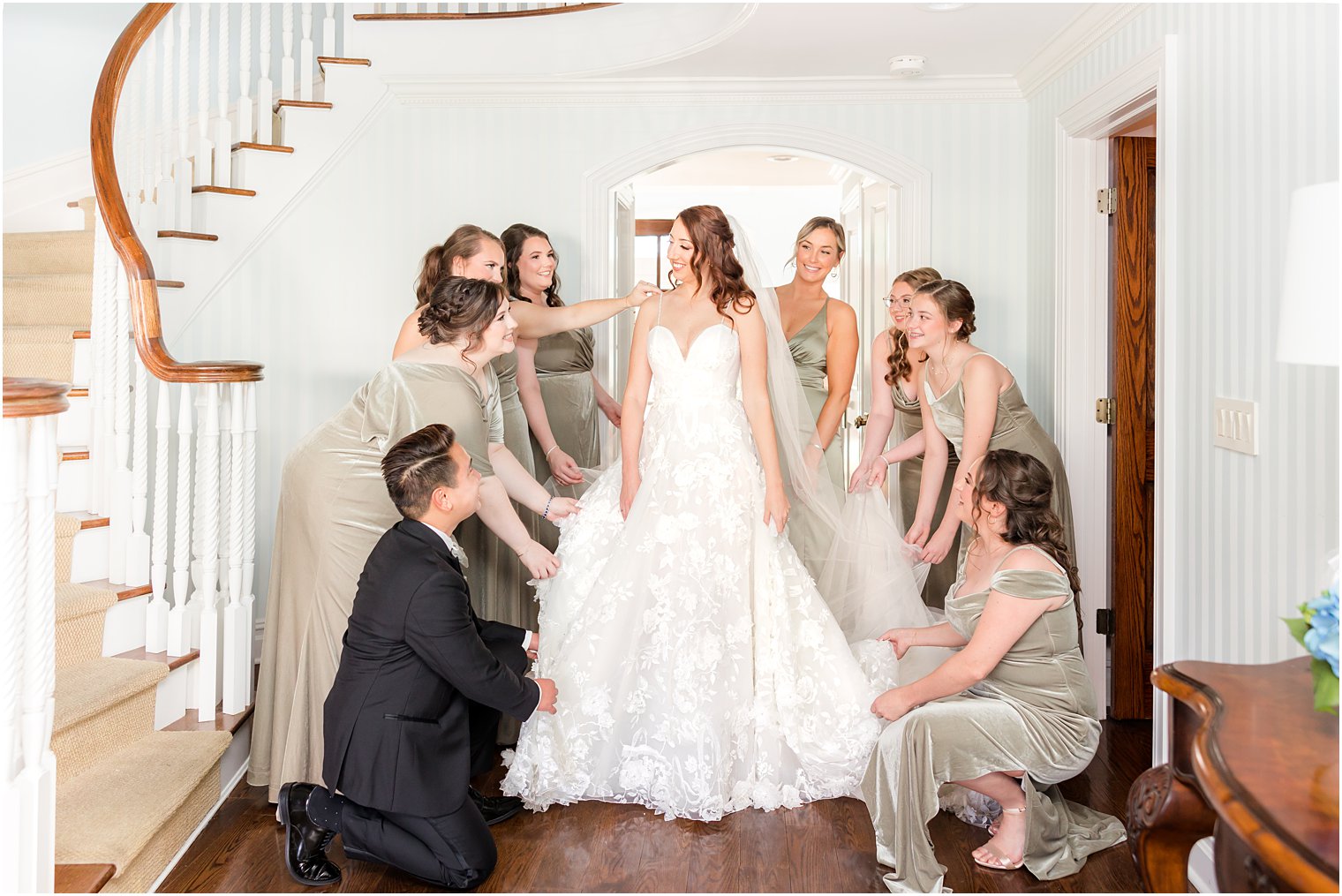 bridal party helps bride with wedding gown inside home 