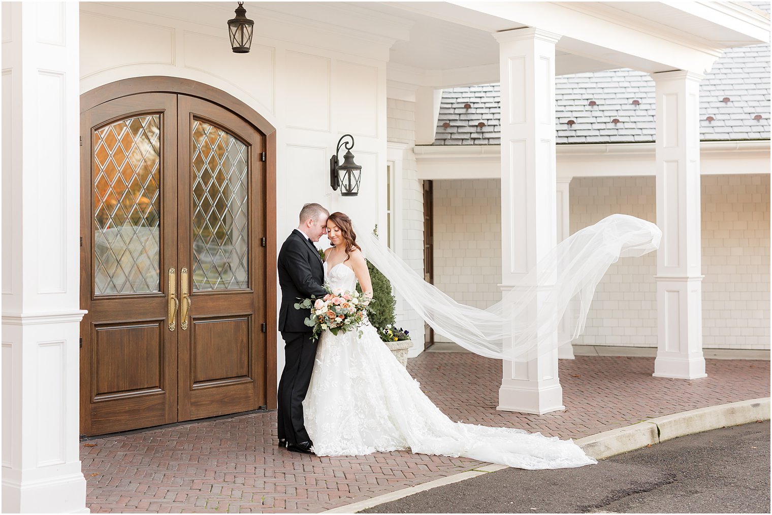 bride and groom kiss outside The Mill Lakeside Manor with bride's veil floating 