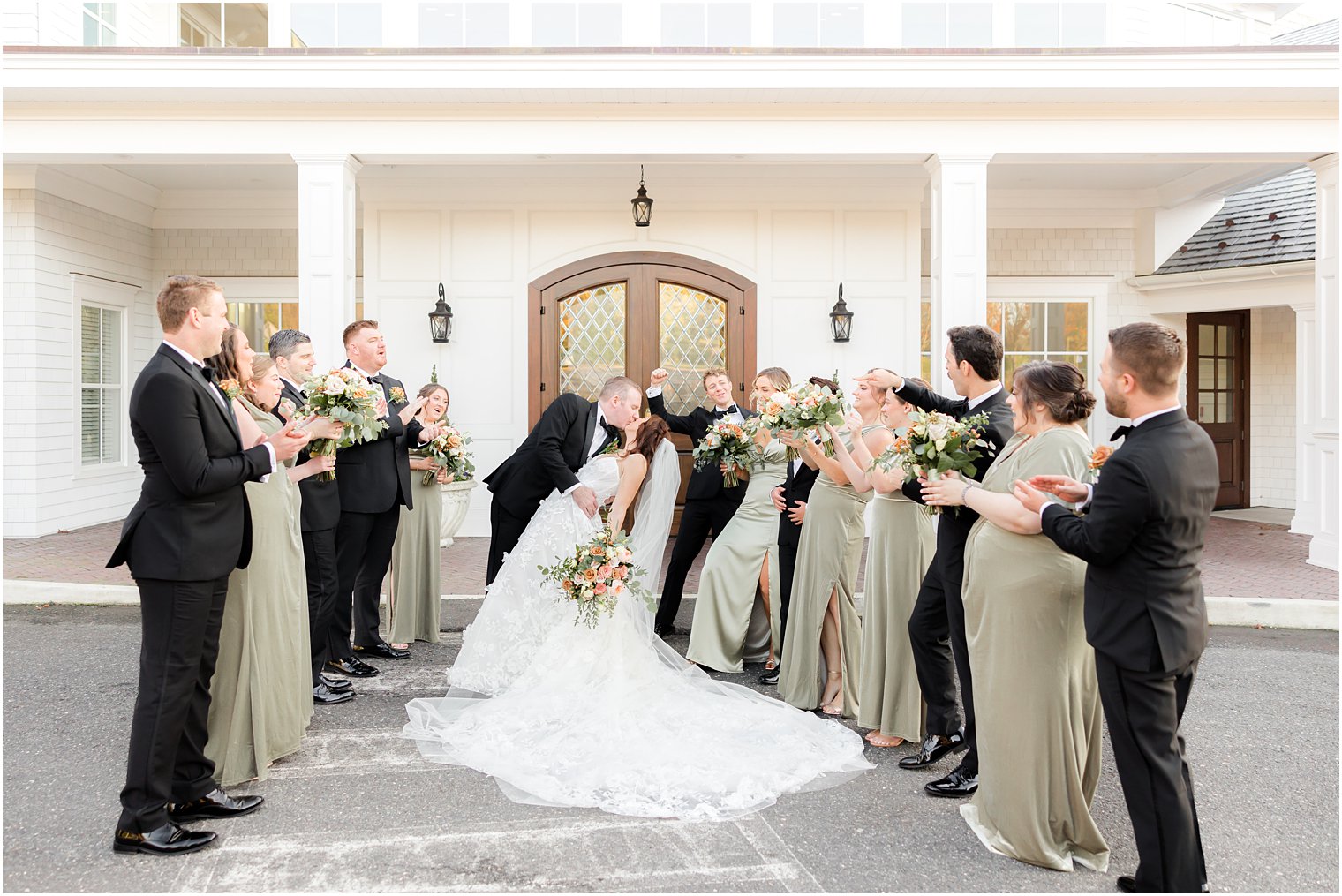 wedding party cheers while groom dips bride kissing her 