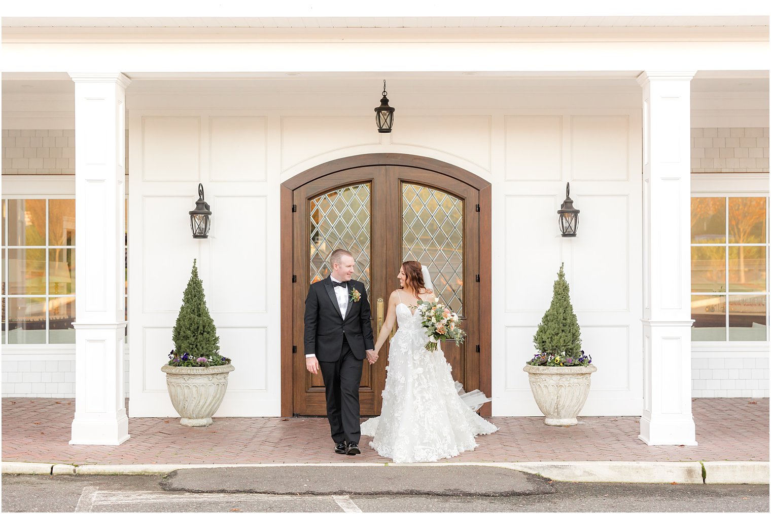 newlyweds hold hands walking by wooden door outside The Mill Lakeside Manor