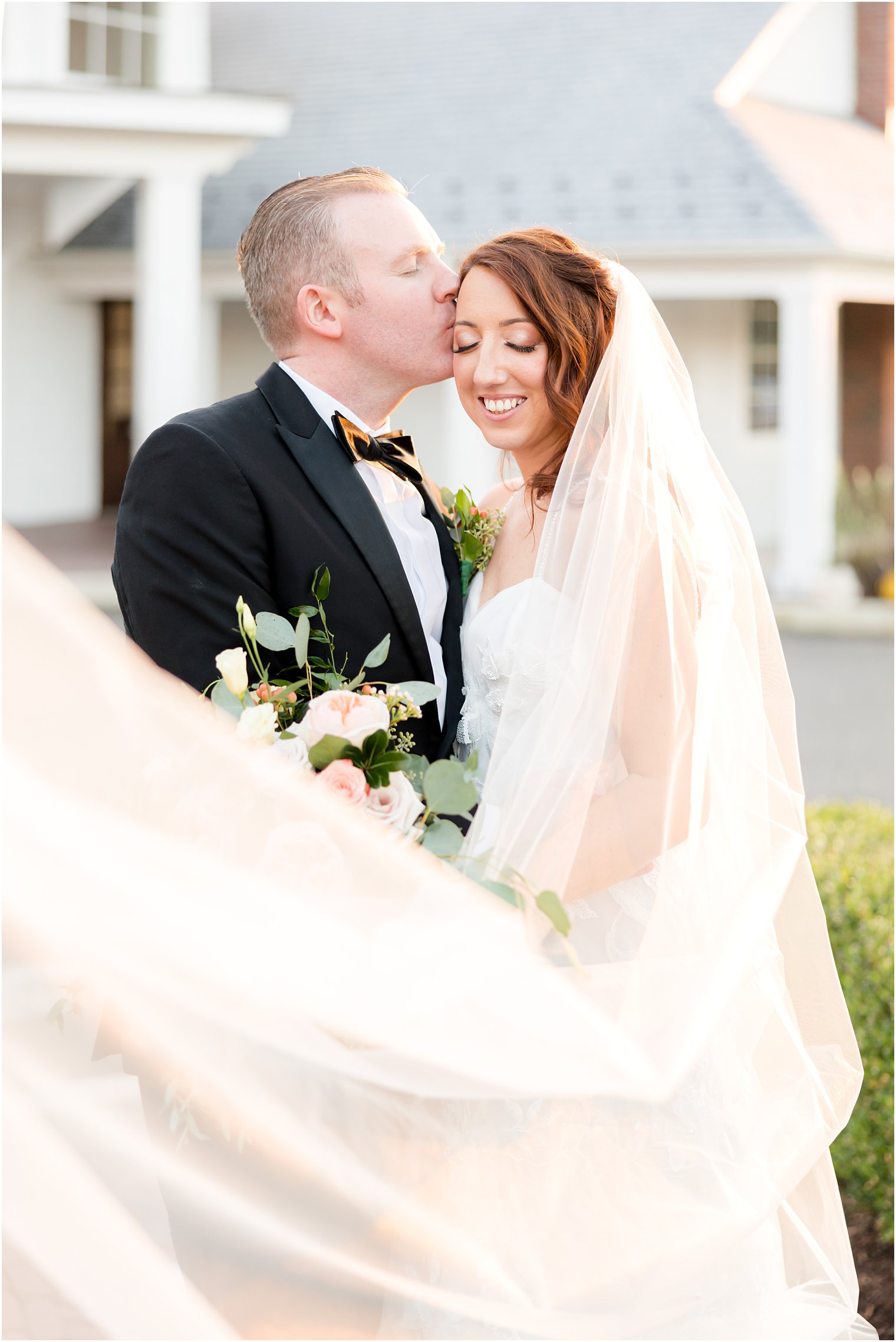 groom kisses bride's forehead with veil wrapped around them at The Mill Lakeside Manor