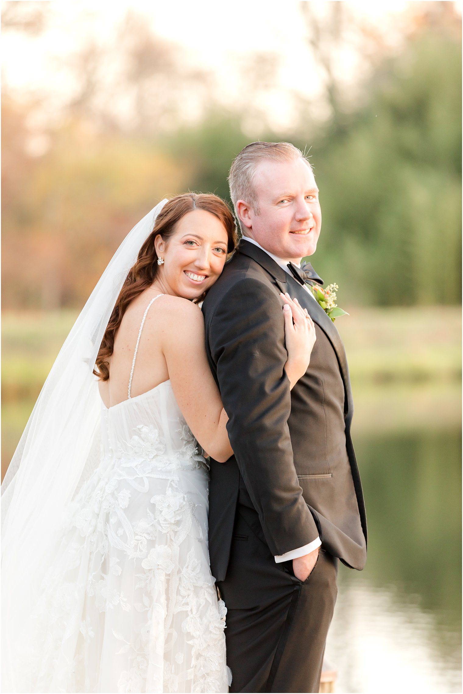 bride hugs groom from behind on dock outside The Mill Lakeside Manor
