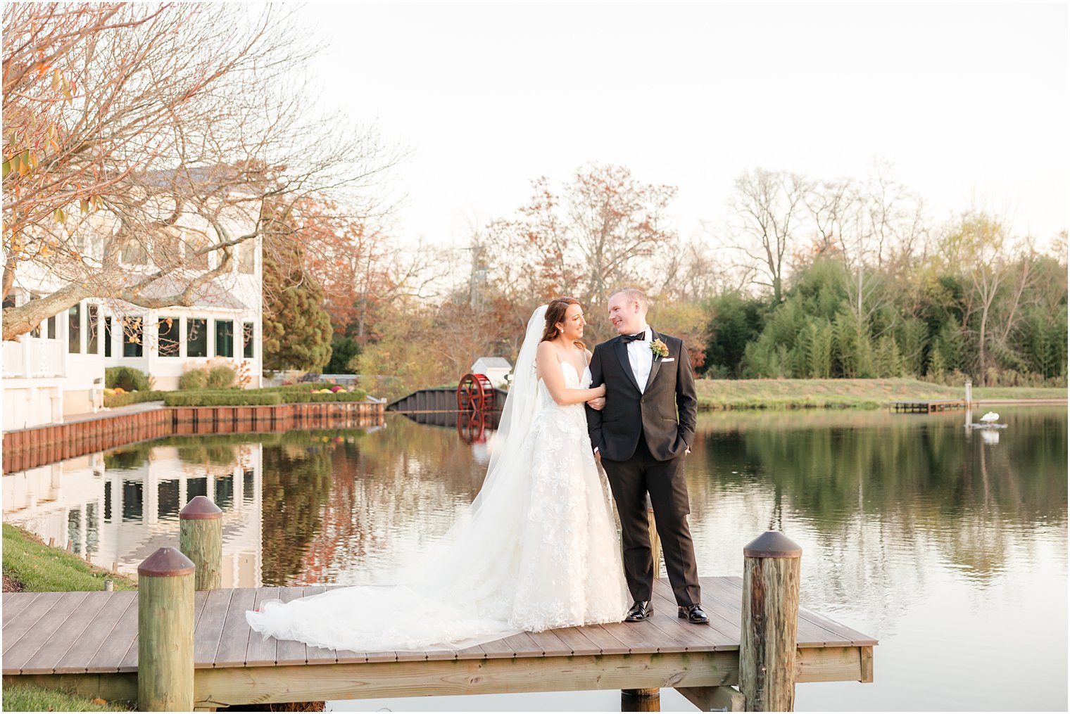 groom looks over at bride standing on dock at The Mill Lakeside Manor