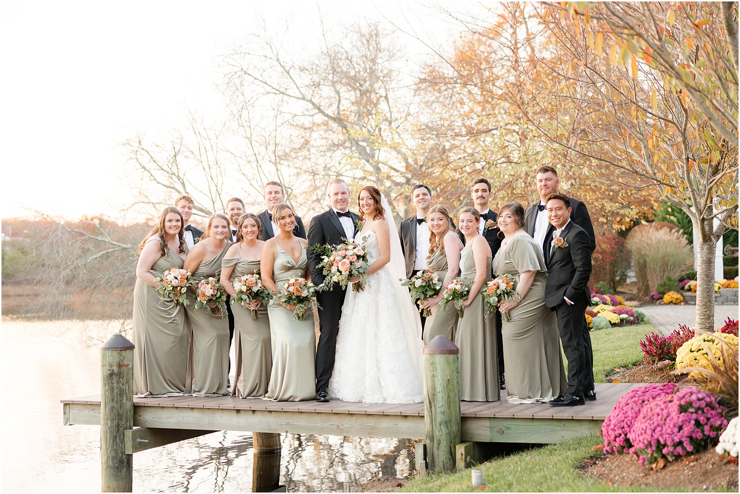 newlyweds stand with wedding party on wooden dock at The Mill Lakeside Manor