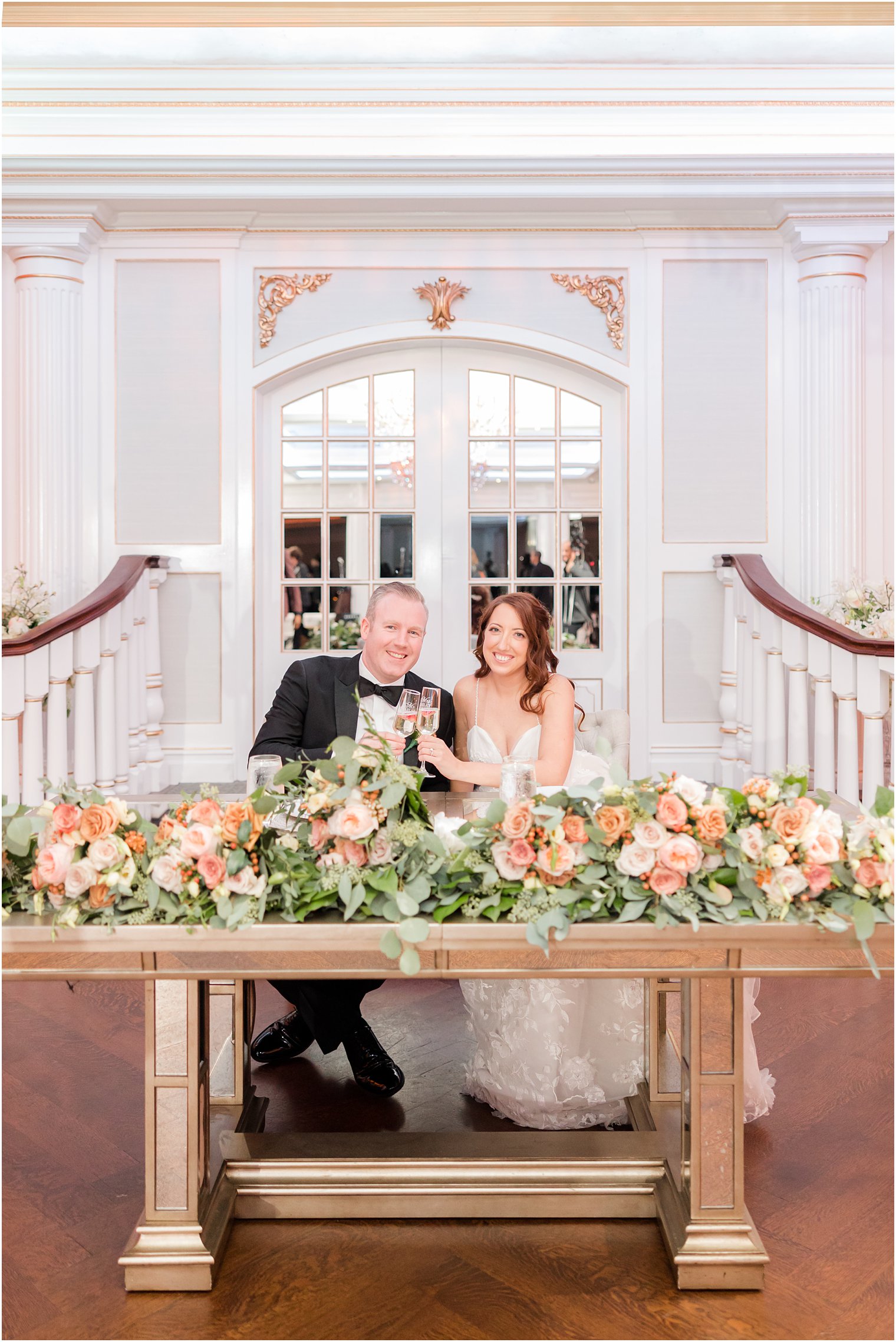 bride and groom sit at sweetheart table with roses draped along front 