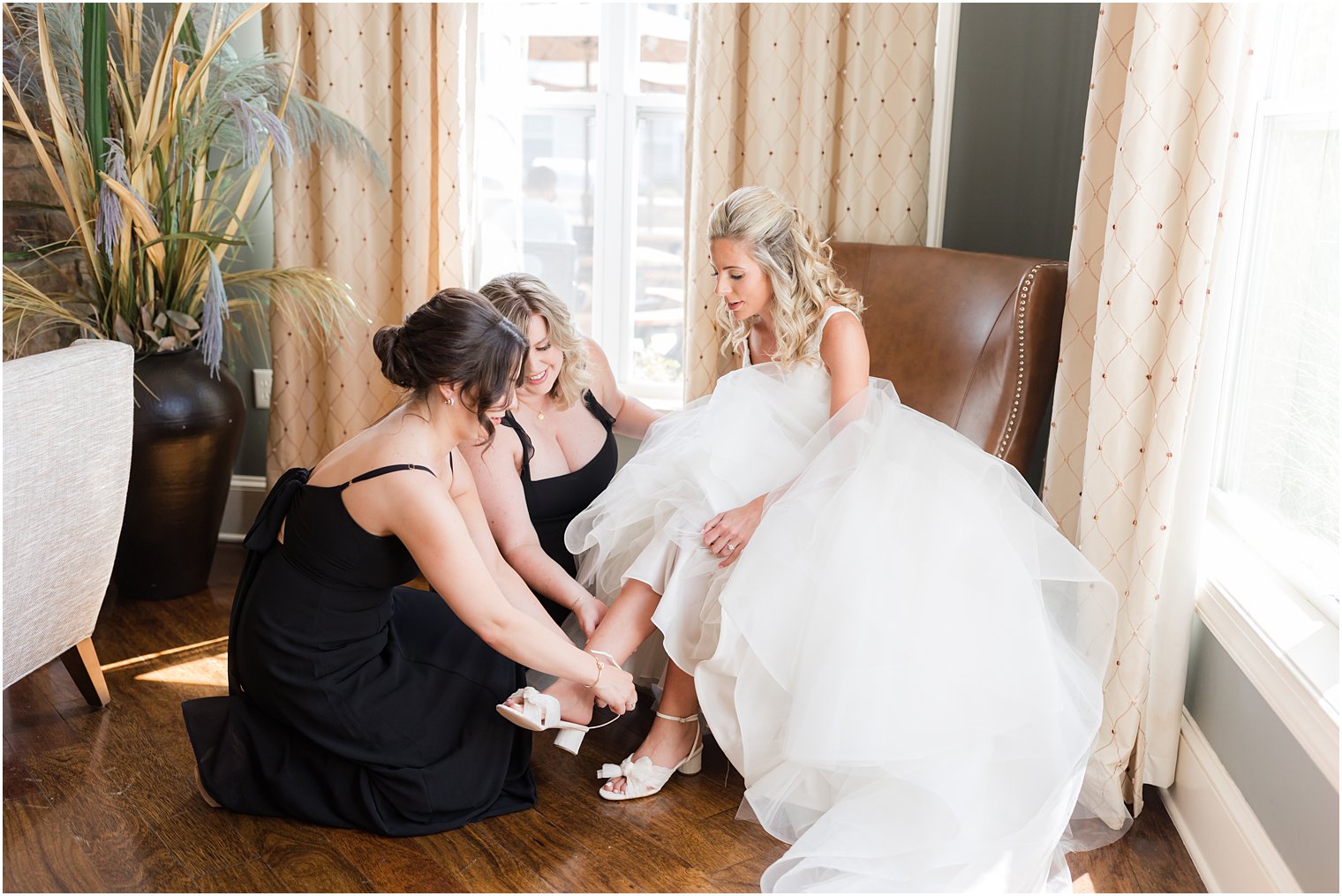 bridesmaids in black dresses help bride with shoes 