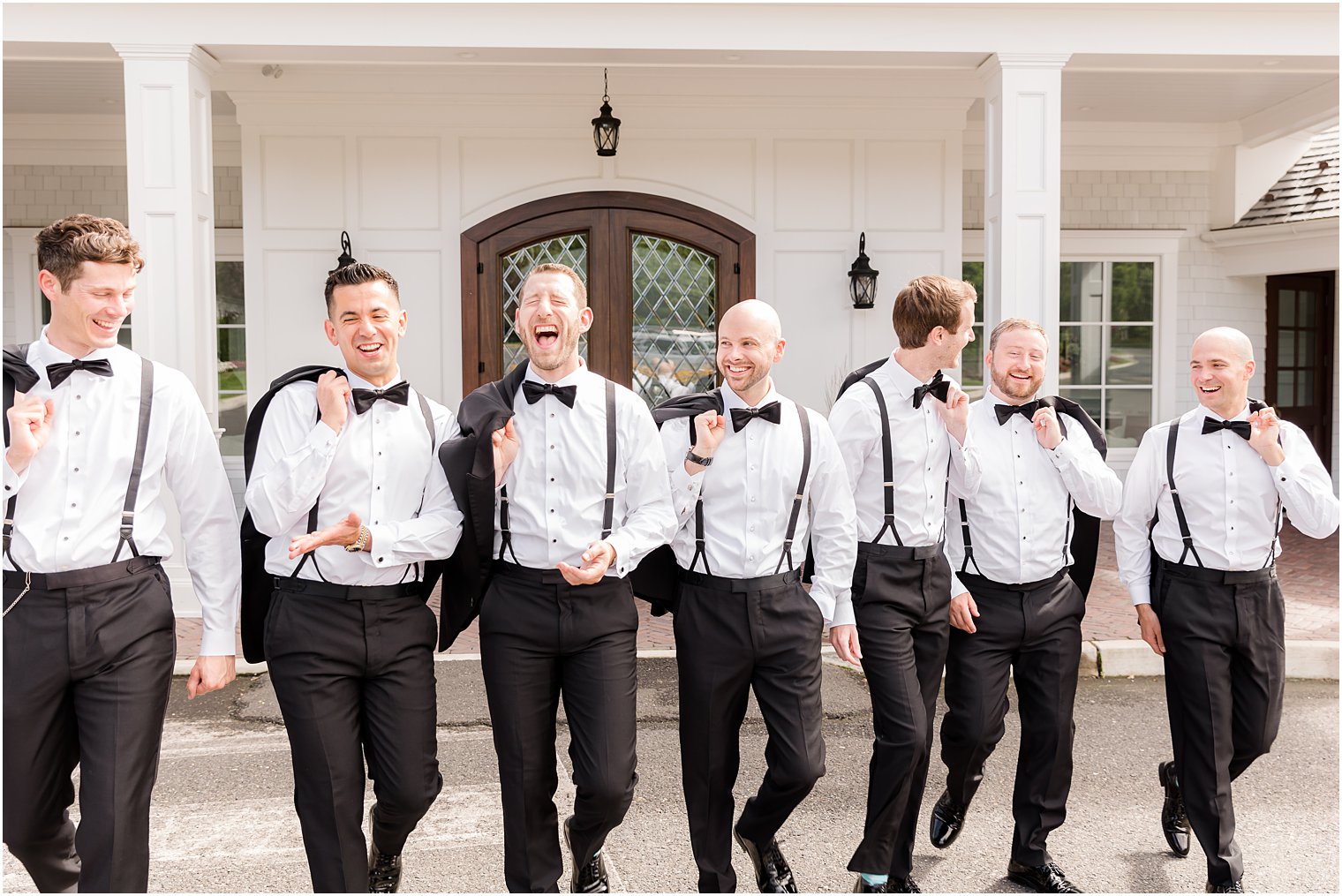 groom and groomsmen walk outside The Mill Lakeside Manor with jackets over shoulders 