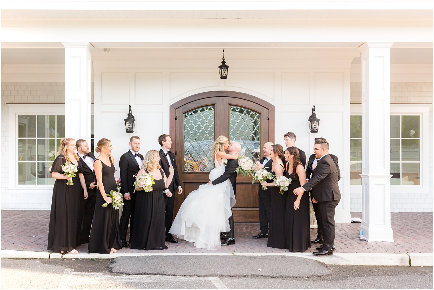 groom lifts up bride standing with wedding party in black outside The Mill Lakeside Manor