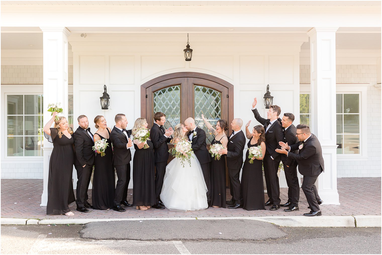 bride and groom kiss while wedding party in black cheers