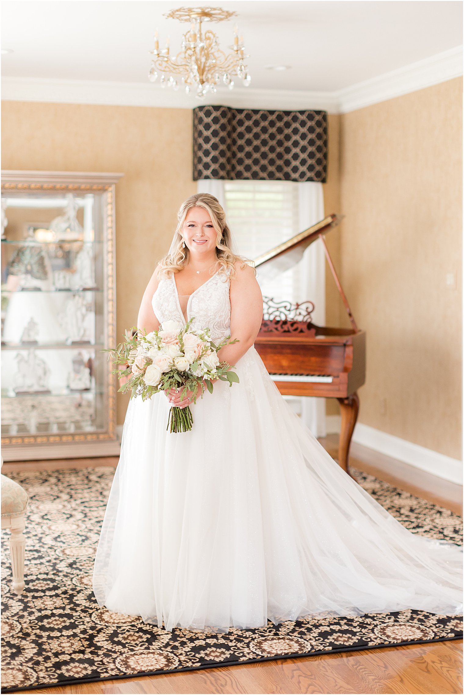 bride stands by piano holding pink and white bouquet
