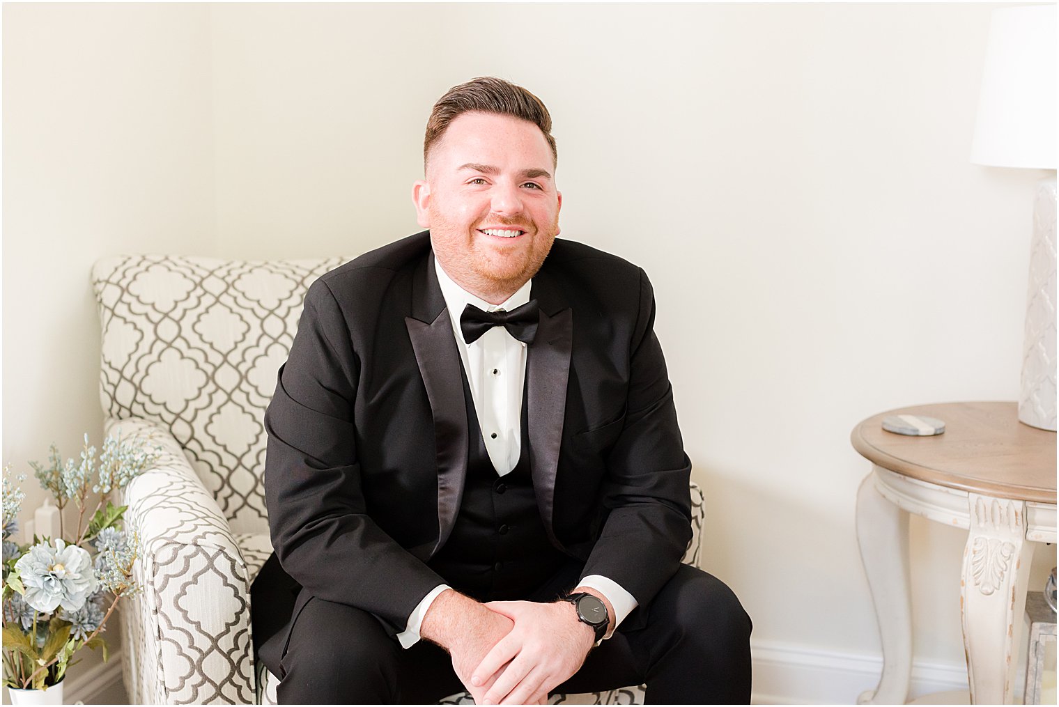 groom sits leaning on knees in classic black suit