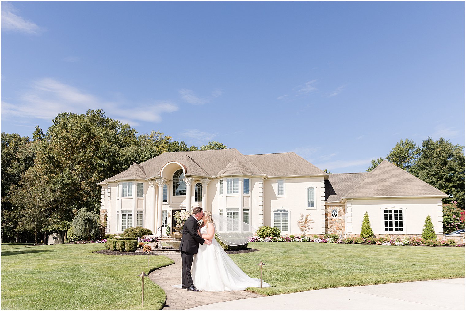 bride and groom kiss outside parents' home with veil floating 