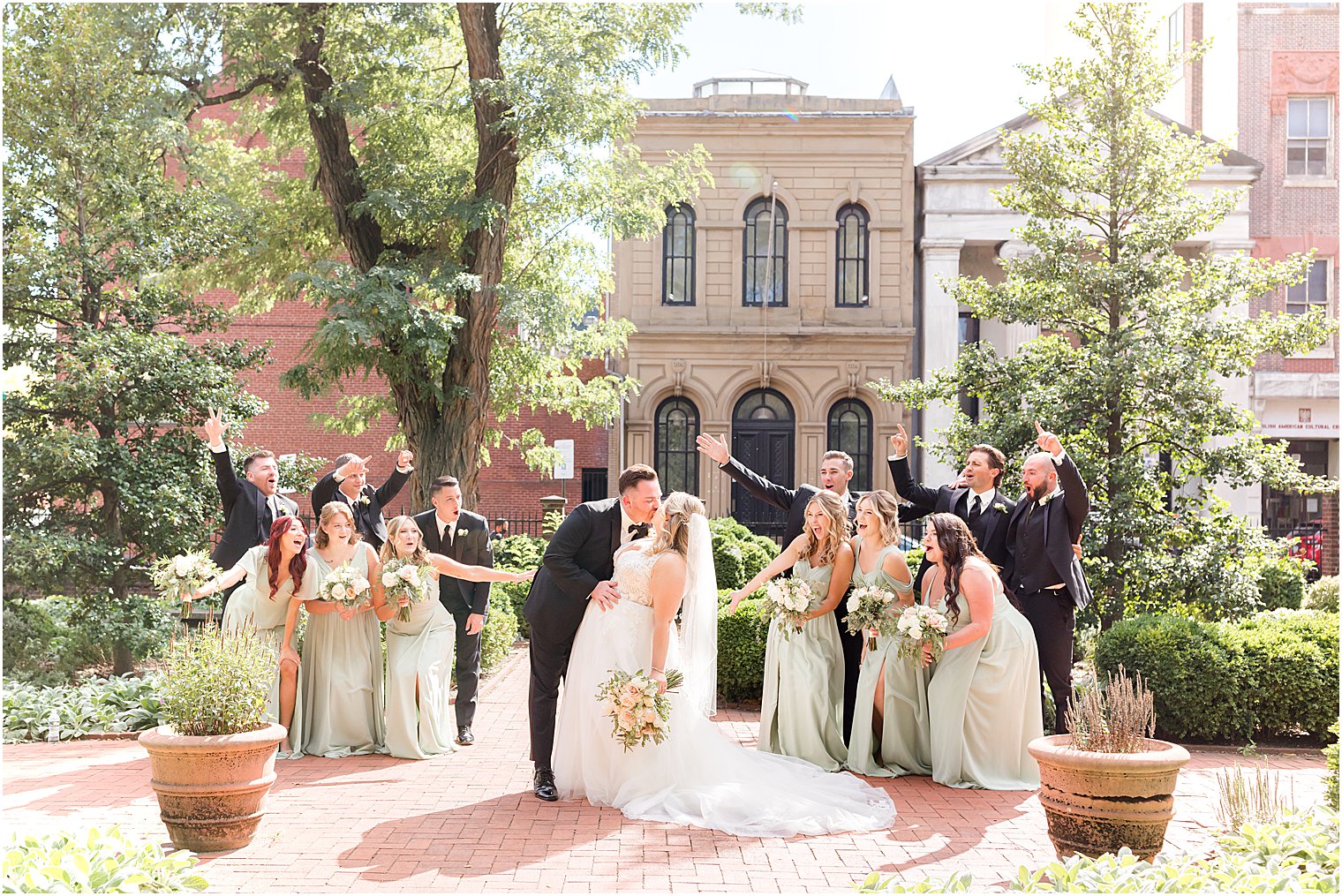 bride and groom kiss outside Benjamin Rush Gardens with wedding party around them 