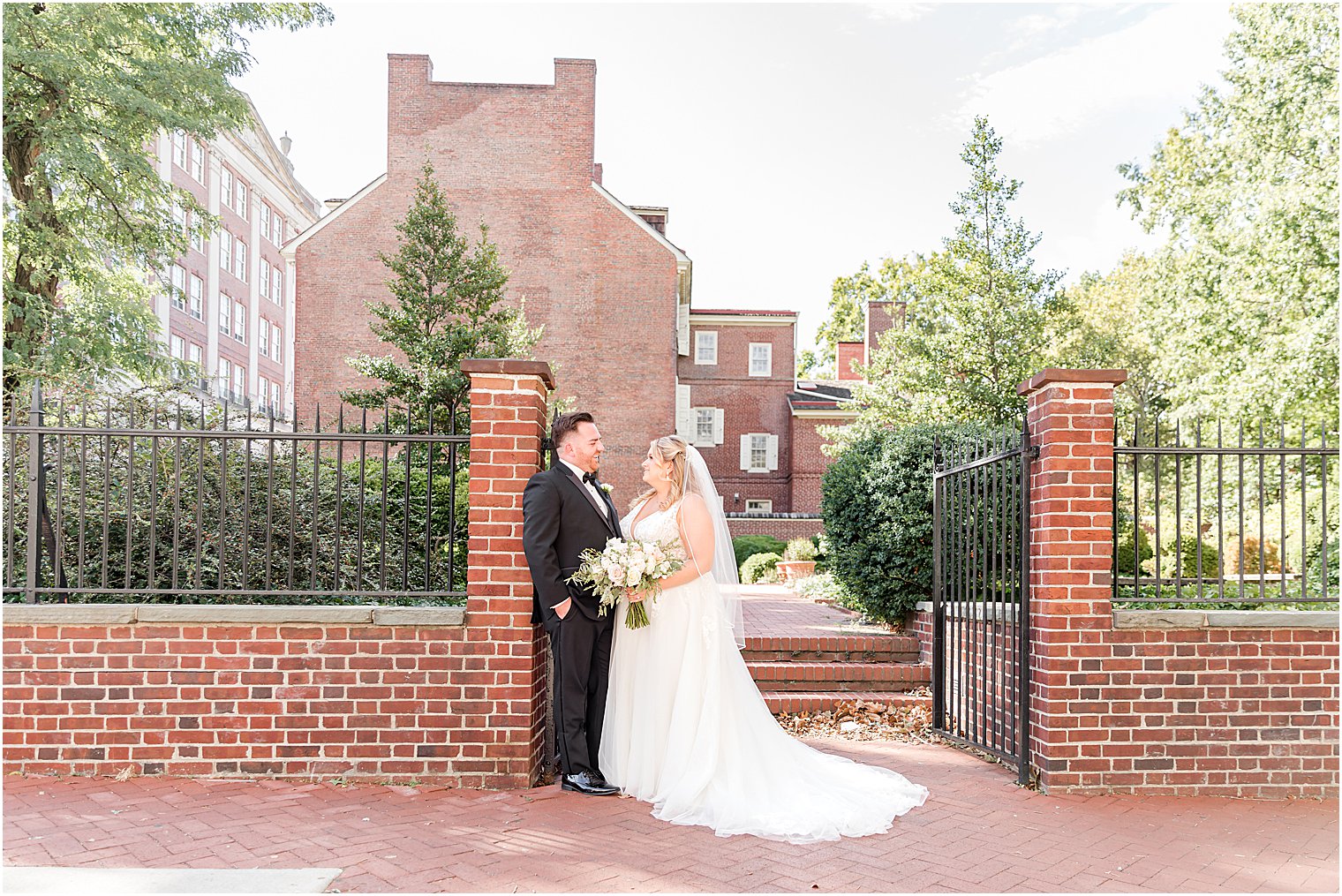 bride and groom lean against brick pillar at Benjamin Rush Gardens