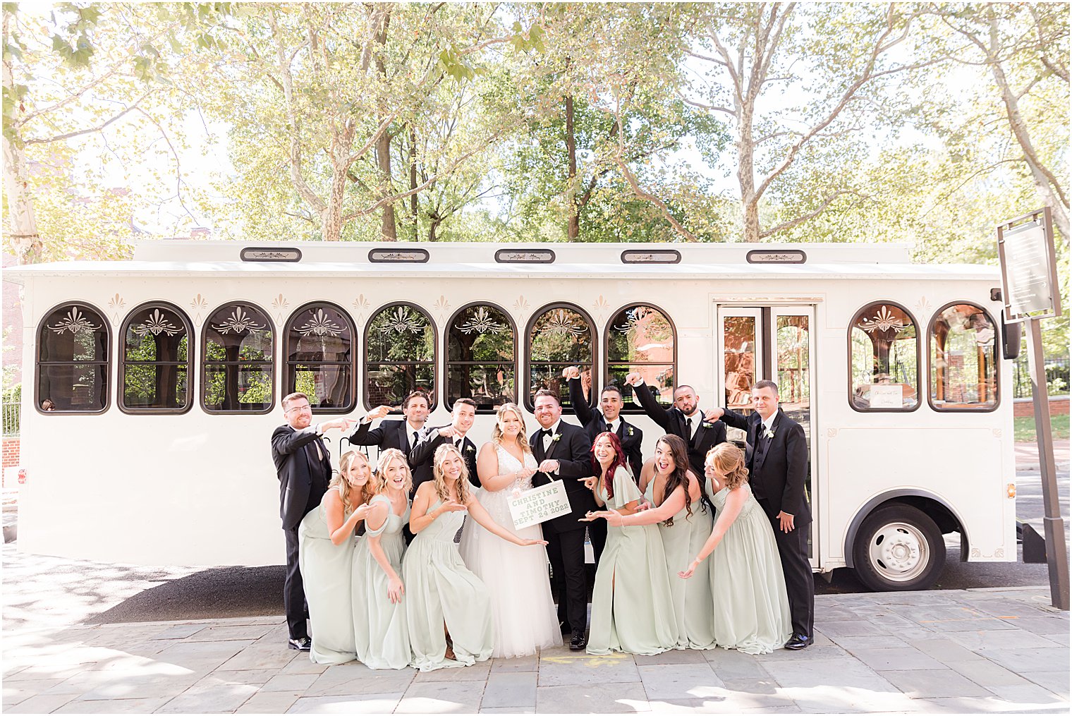 bride and groom laugh hugging with bridal party outside white trolley in Philly PA