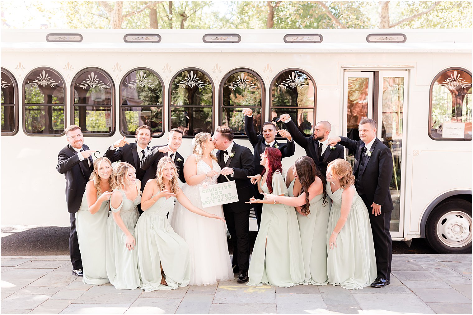 bride and groom laugh hugging with bridal party outside white trolley in Philly PA