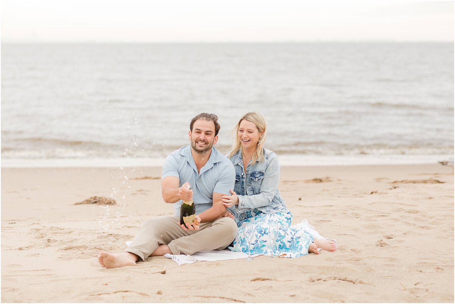 bride sits with groom pouring champagne during Union Beach engagement session 