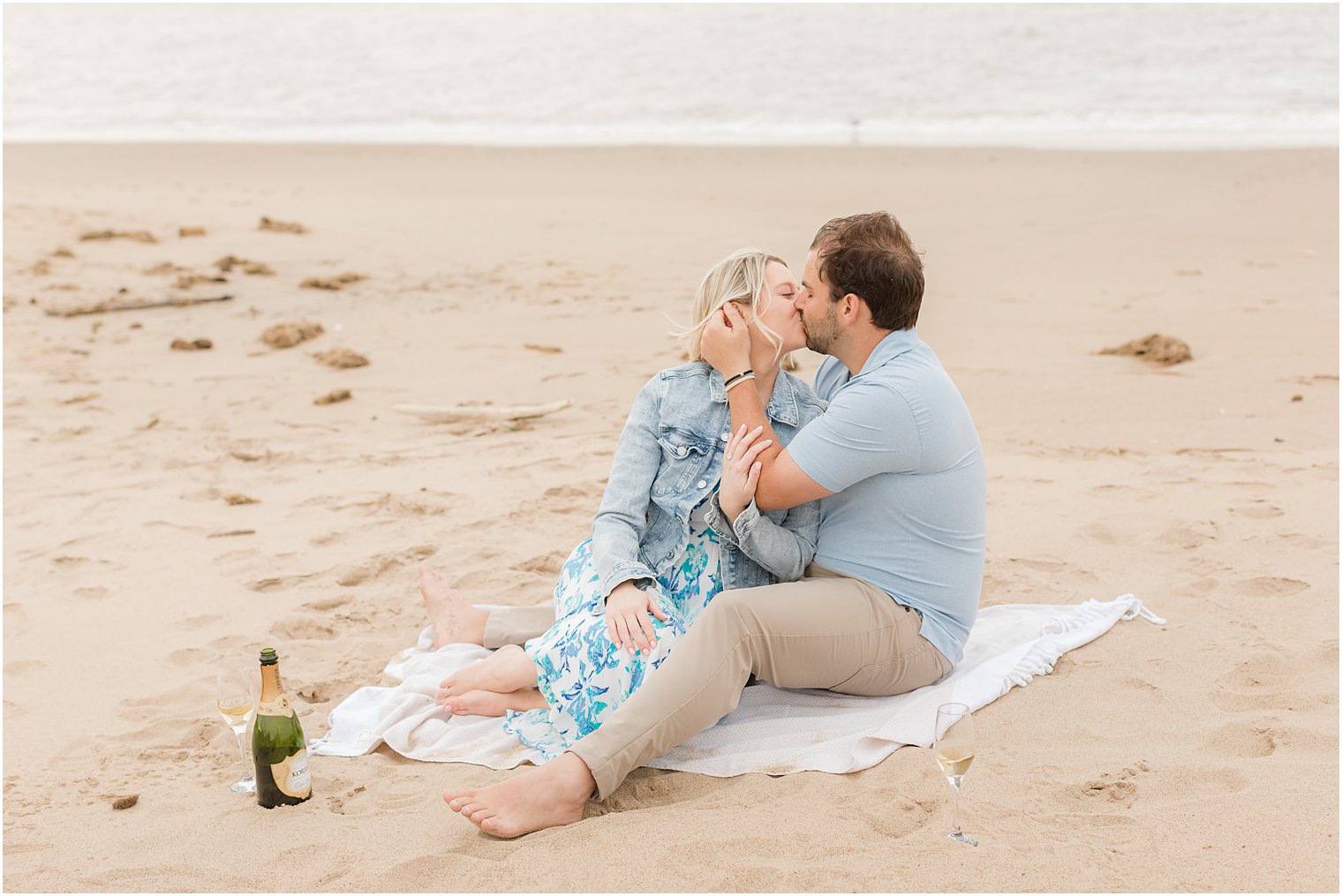 engaged couple kisses on blanket during beach engagement photos 