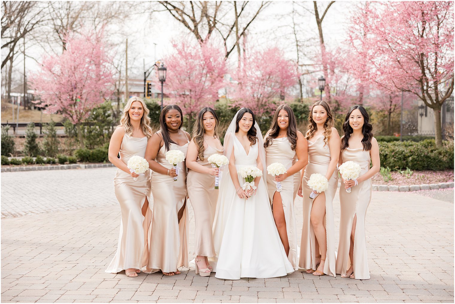 bride stands with bridesmaids by pink trees outside Nanina's in the Park