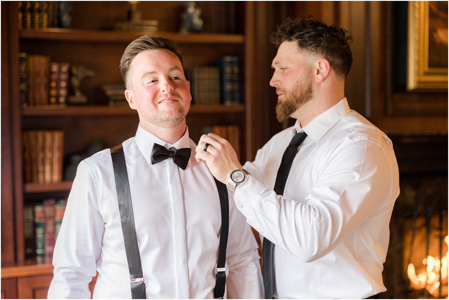 groomsman adjusts bowtie for groom in library at Nanina's in the Park