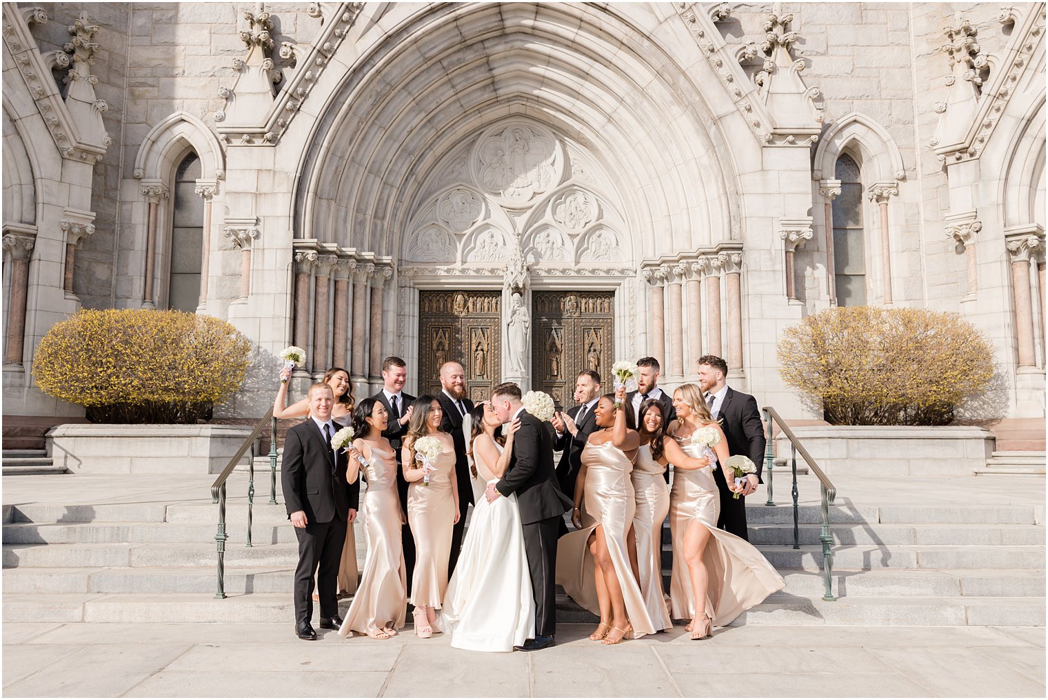 bride and groom kiss with wedding party around them outside at The Cathedral Basilica of the Sacred Heart 