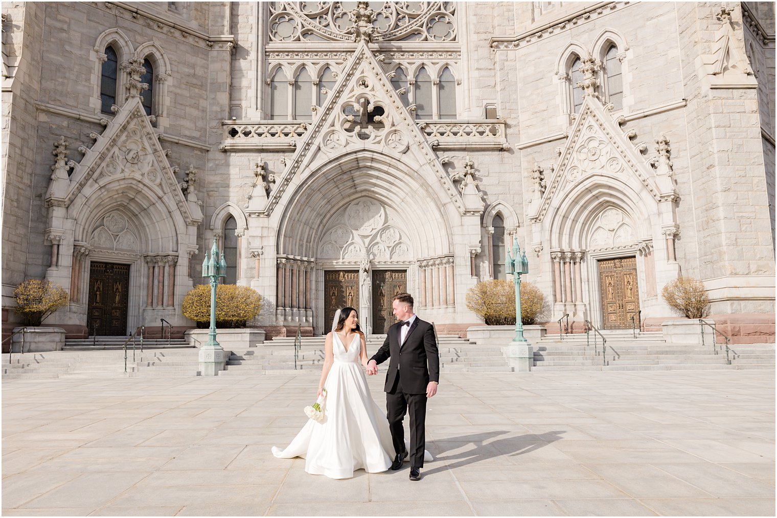 bride and groom hold hands walking outside The Cathedral Basilica of the Sacred Heart